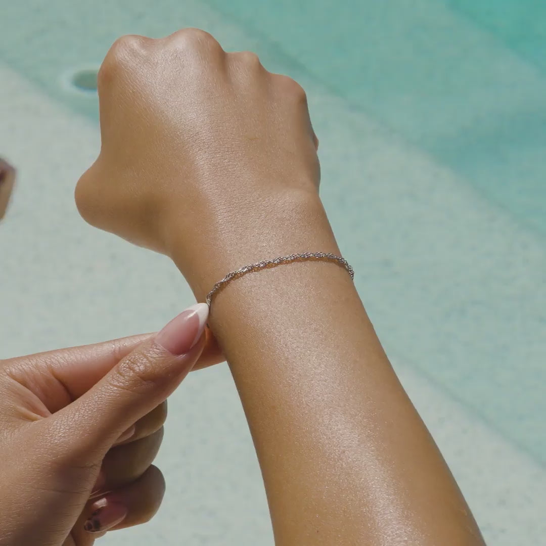 video of a stainless steel singapore chain bracelet with an extender on a model at the pool with french tip nails