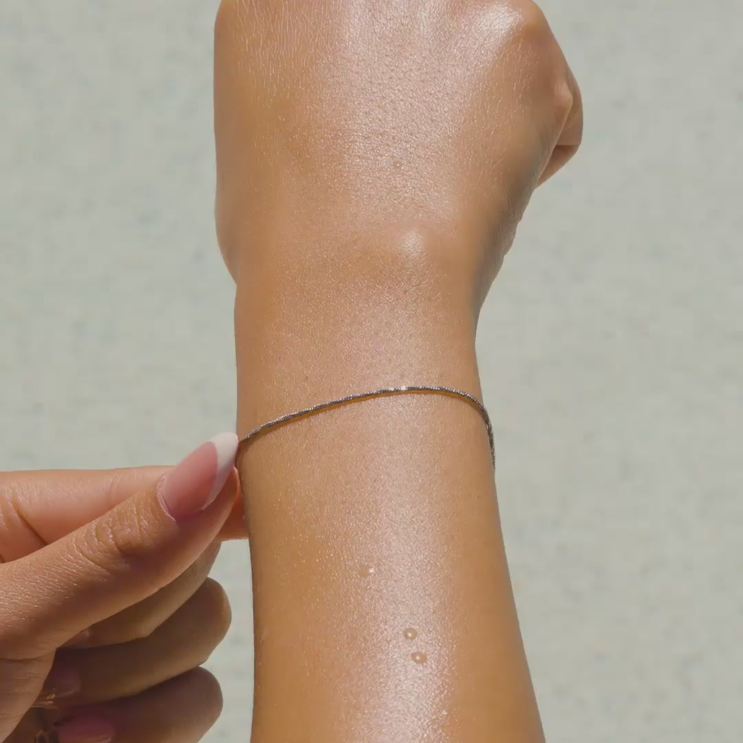 a video of a silver stainless steel dainty snake chain bracelet on a model with french tip nails by the pool
