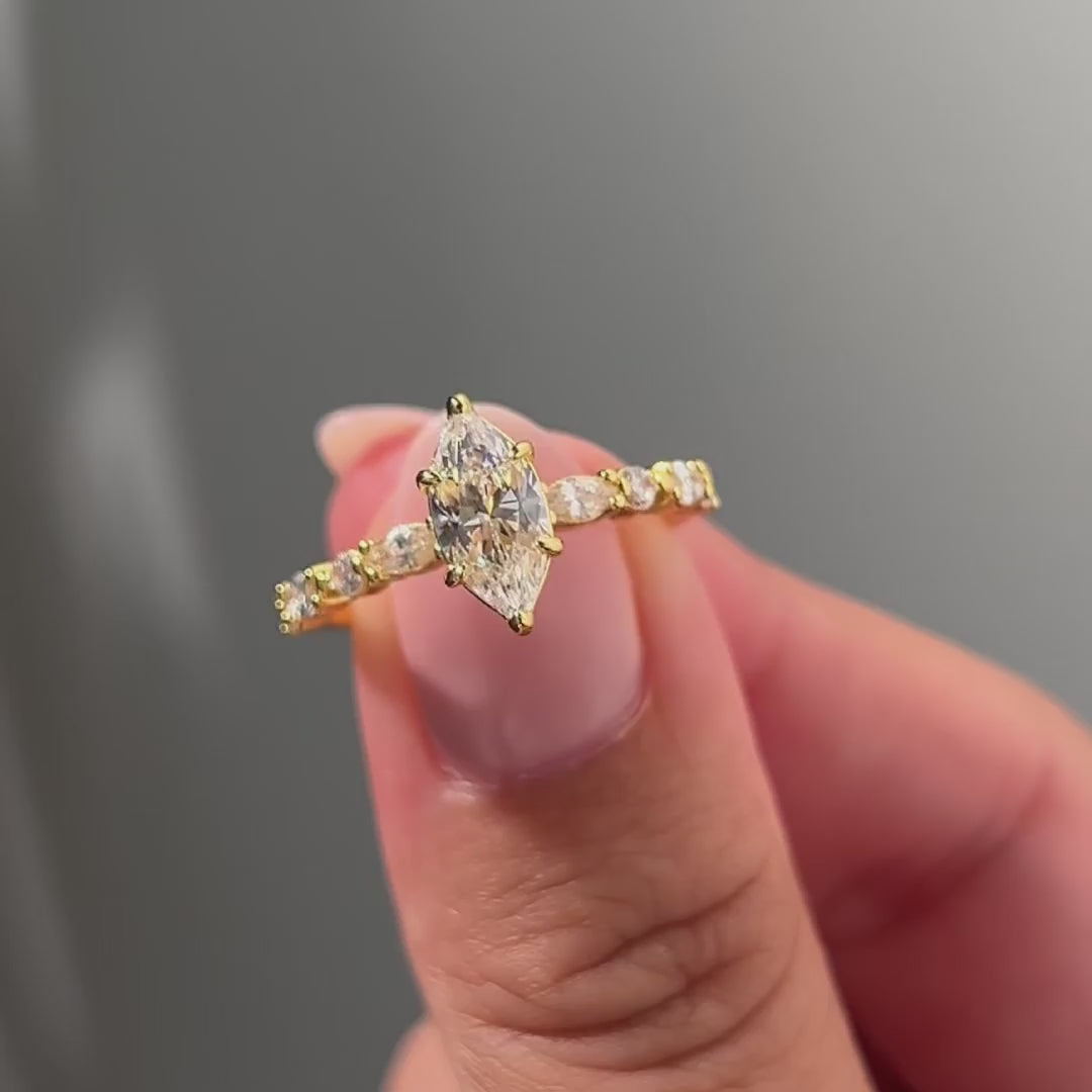video of gold 1 carat marquise cut half eternity engagement ring held by model with light pink nails