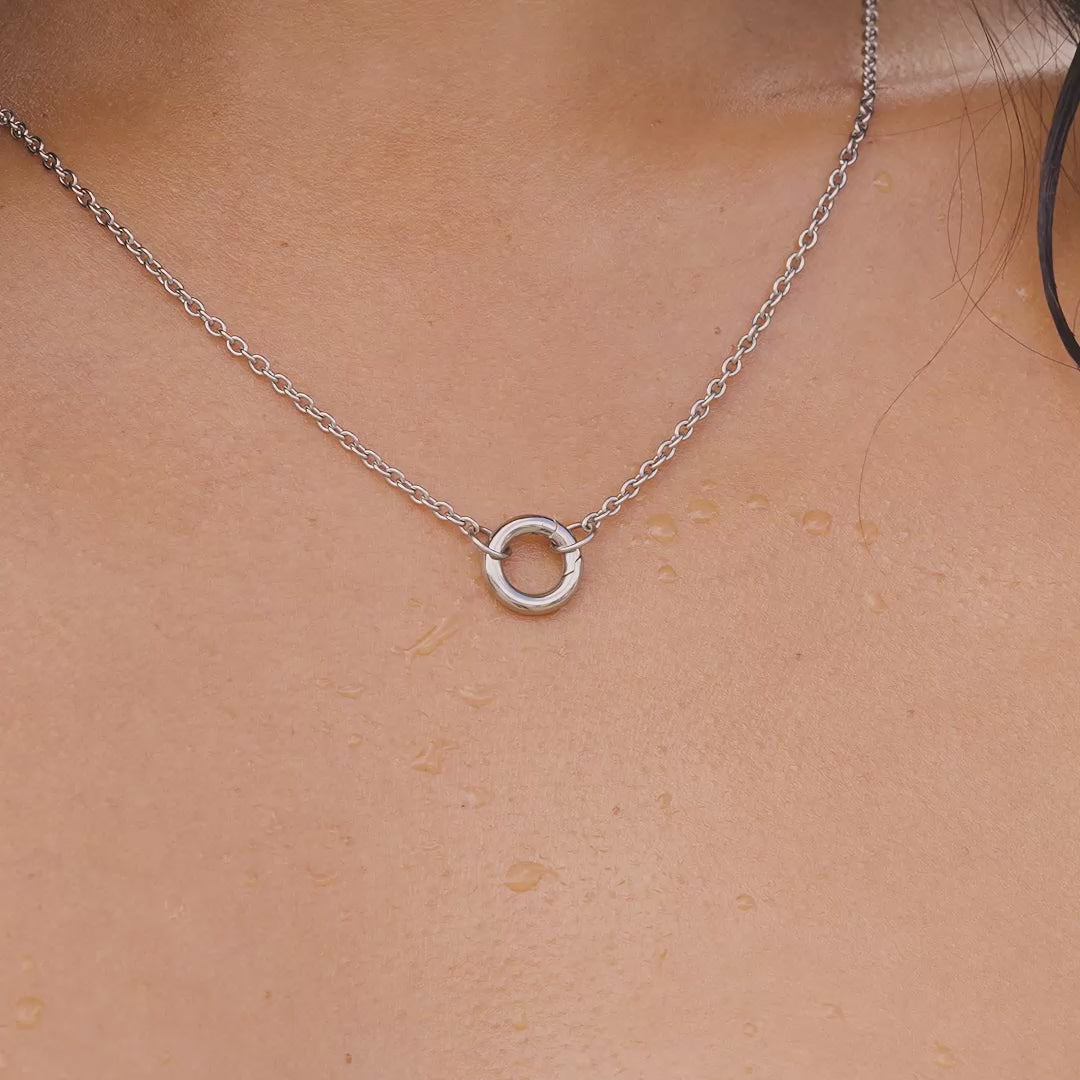 video of a silver stainless steel charm necklace on a model by the pool
