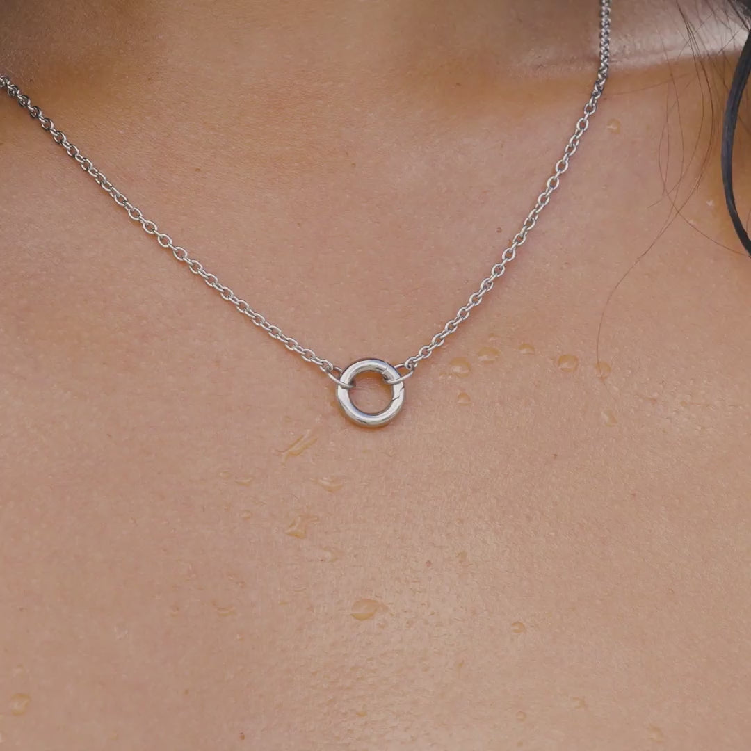video of a silver stainless steel charm necklace on a model by the pool