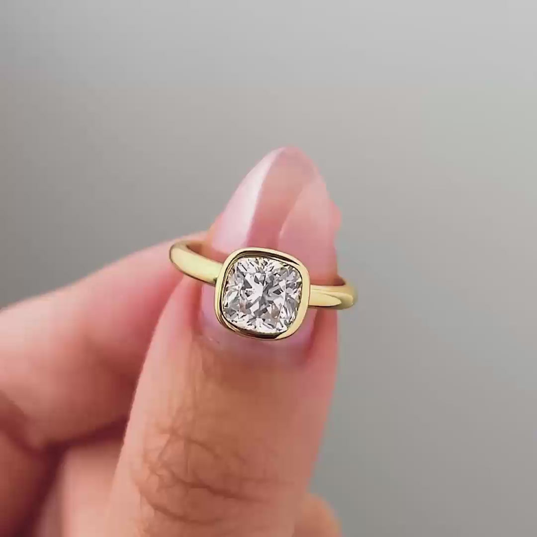 a video compilation of a gold cushion cut bezel engagement ring shown in different settings by a model with pink manicured nails