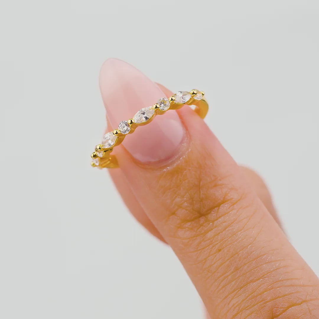 gold wedding band with round and marquise stones held by model on white background