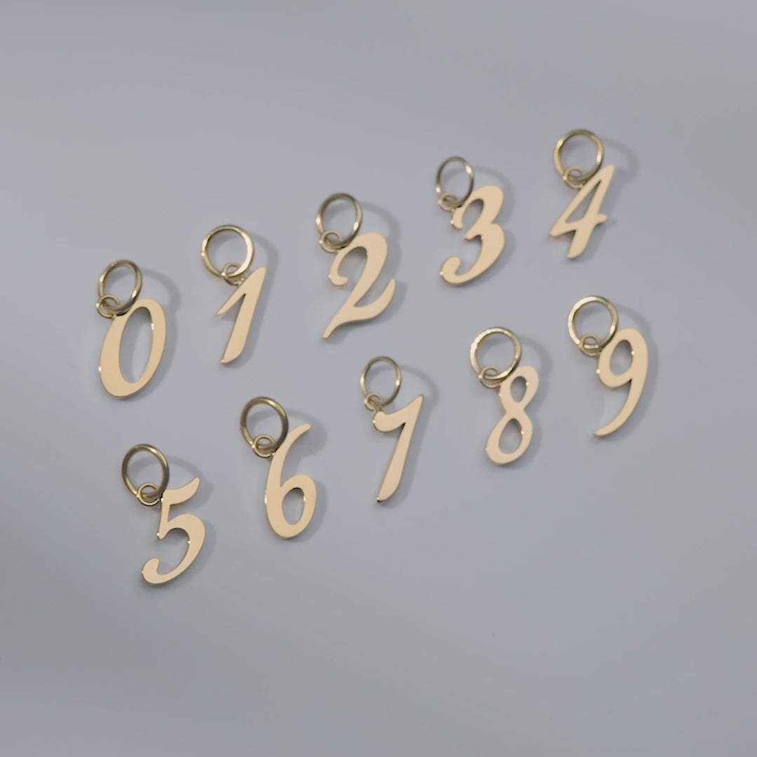 video of gold stainless steel number charms 0-9 shown in flatlay version and attached to a charm necklace and bracelet