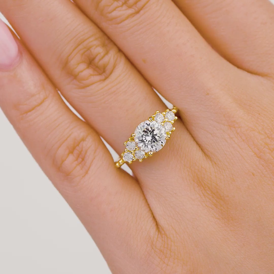 video of gold 1.75 carat round cut engagement ring with three dainty round stones on either side on model