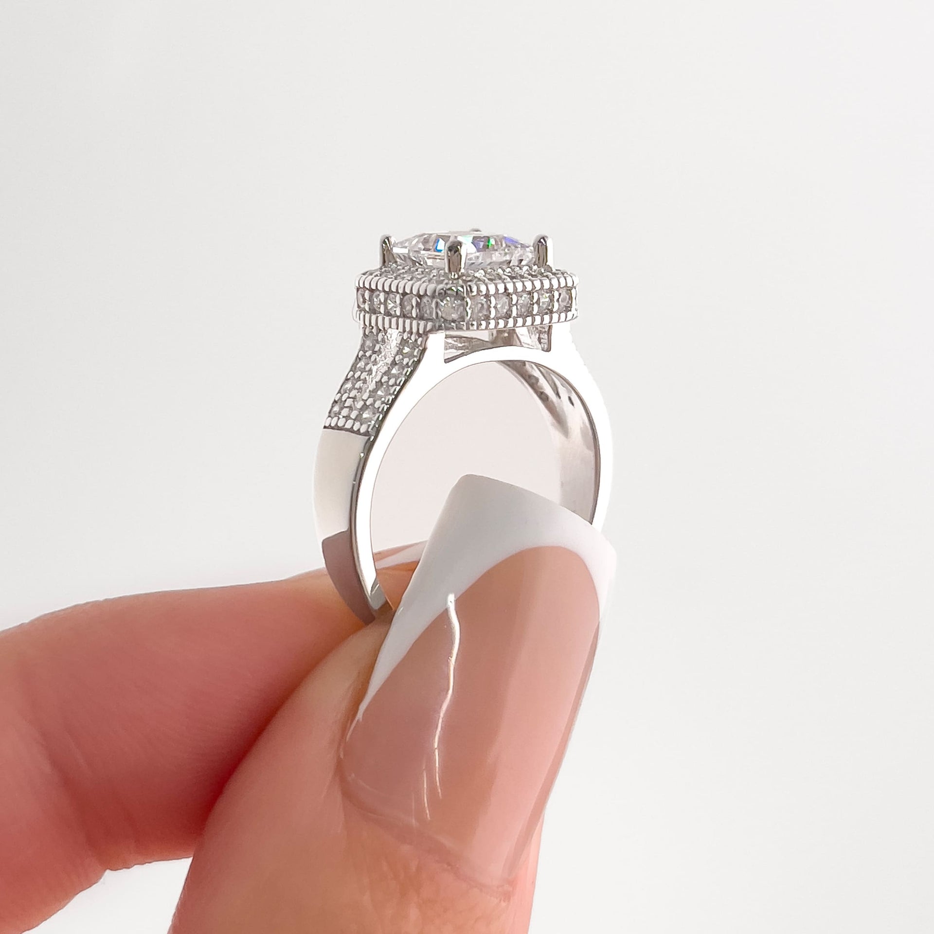 setting shot of split shank princess cut engagement ring held by female with french tip