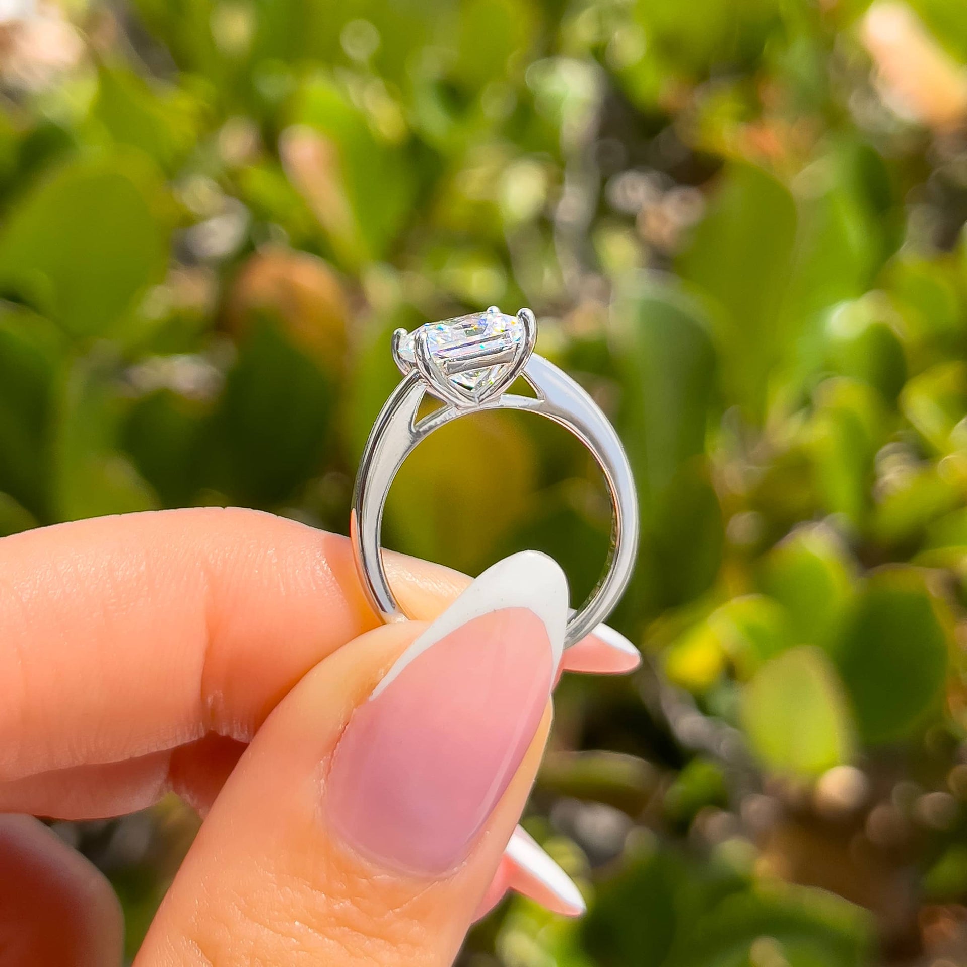 setting view of a silver solitaire princess cut engagement ring in hand with french tip nails