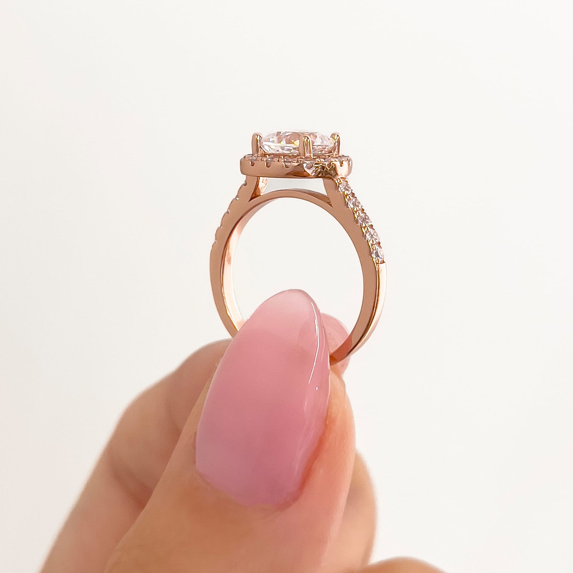 setting shot of rose gold cushion halo engagement ring held by model with neutral nails