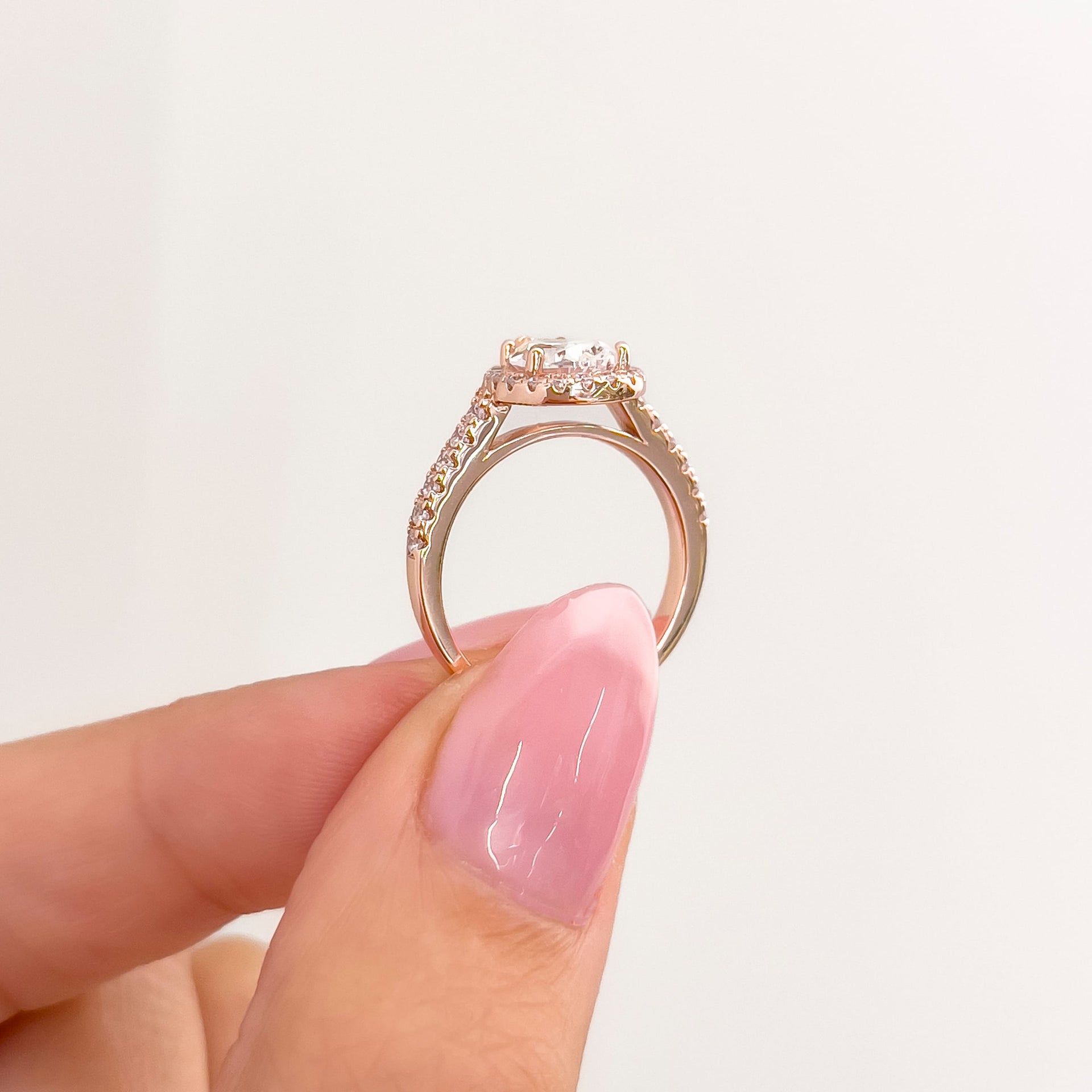 setting shot of rose gold pear cut halo engagement ring held by model with pink nails