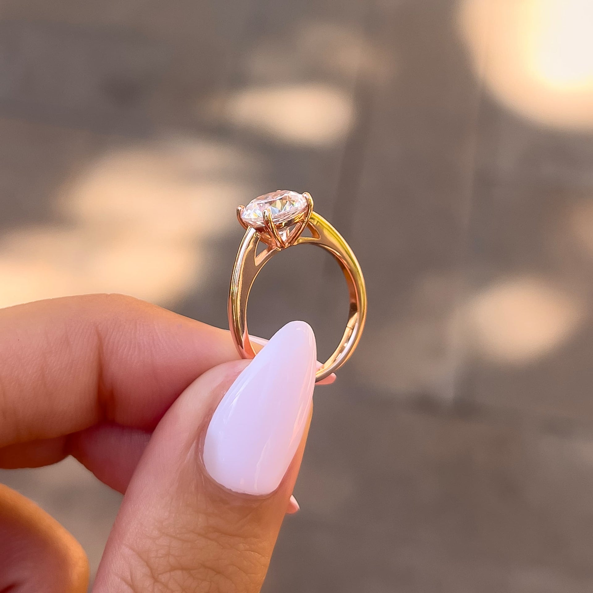 side profile of rose gold round cut solitaire engagement ring held by model with light pink nails