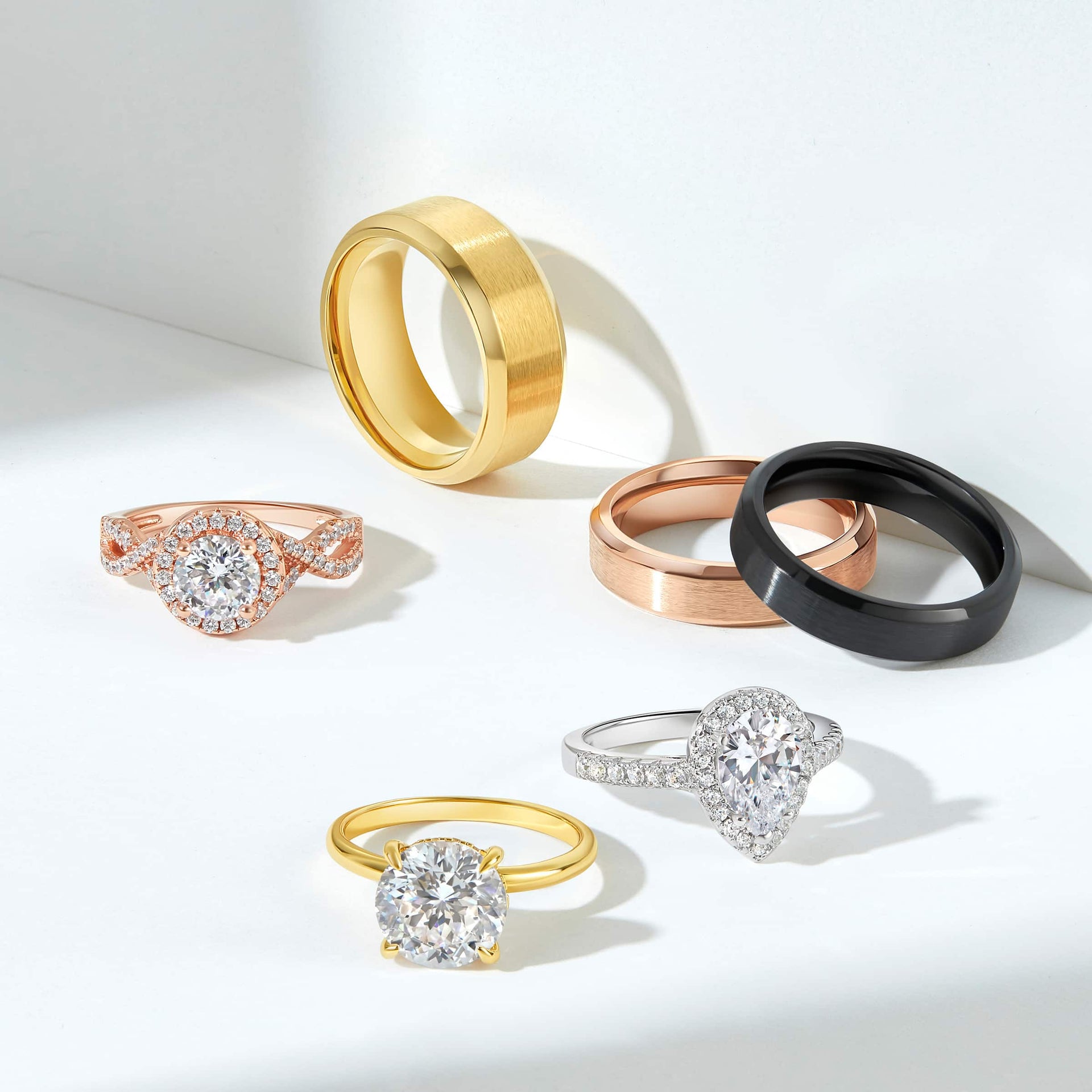 multiple mens and women's wedding rings in silver, rose gold, gold, and black shown on an off-white background