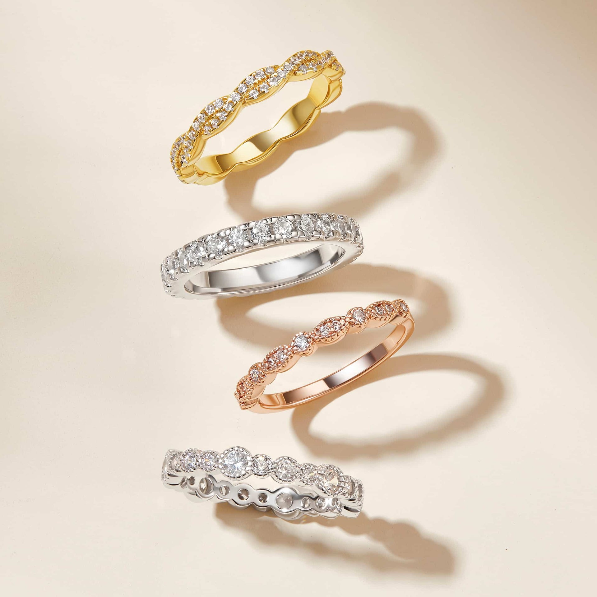 a gold wedding band, a rose gold wedding band, and two silver wedding bands all on a cream colored background