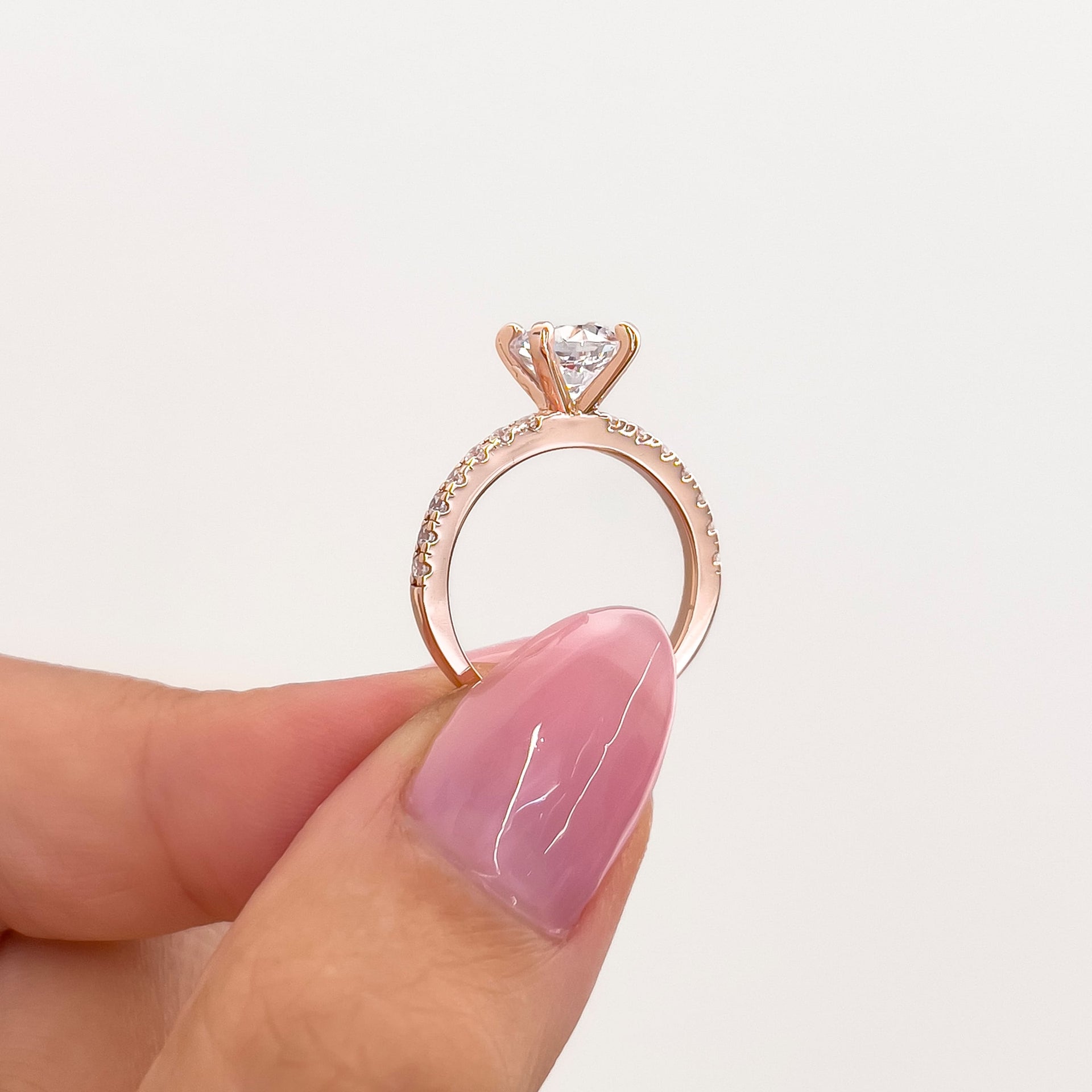 setting shot of rose gold 1.75 carat round cut engagement ring held by model with pink nails