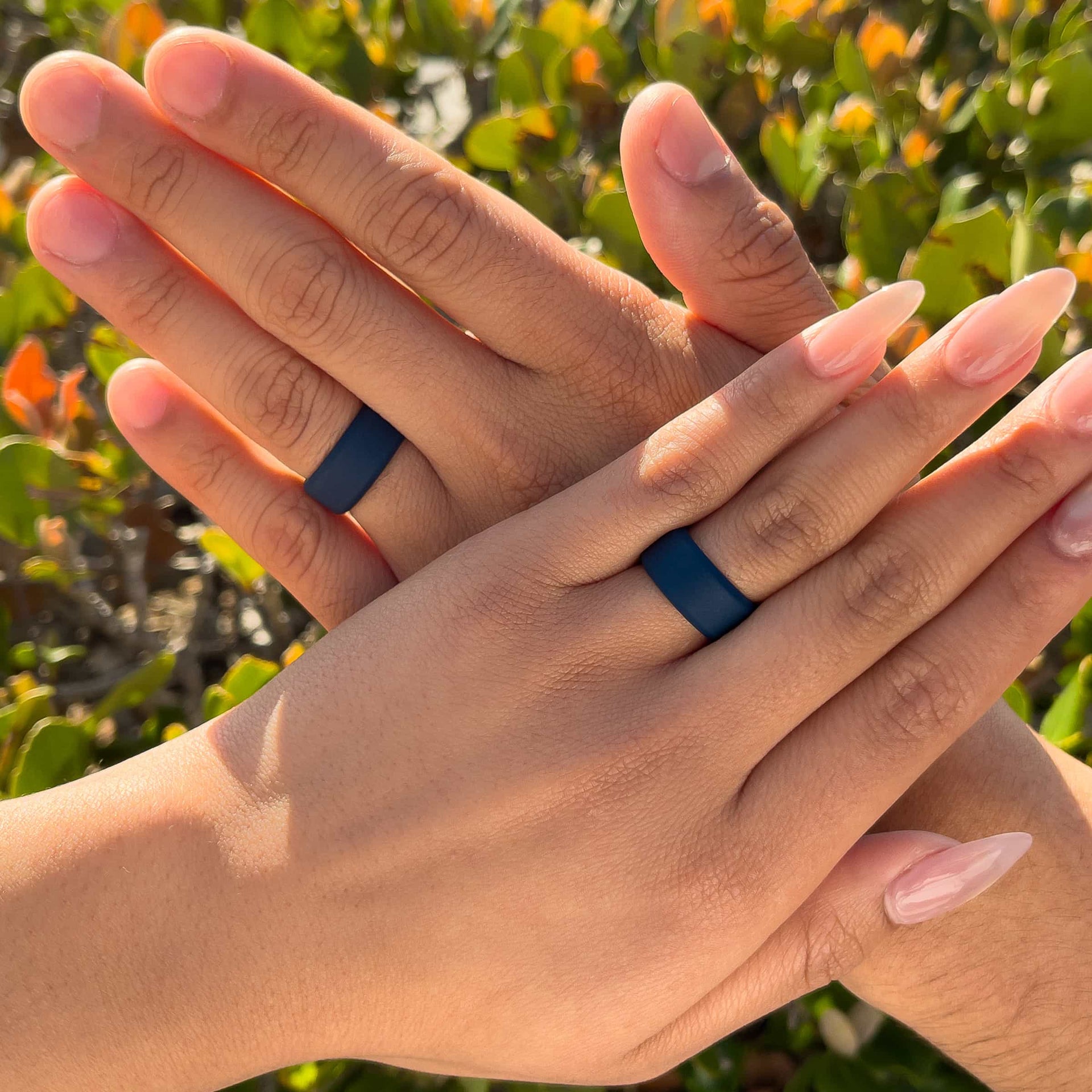 a male and female model wearing matching dark blue silicone wedding bands in front of greenery