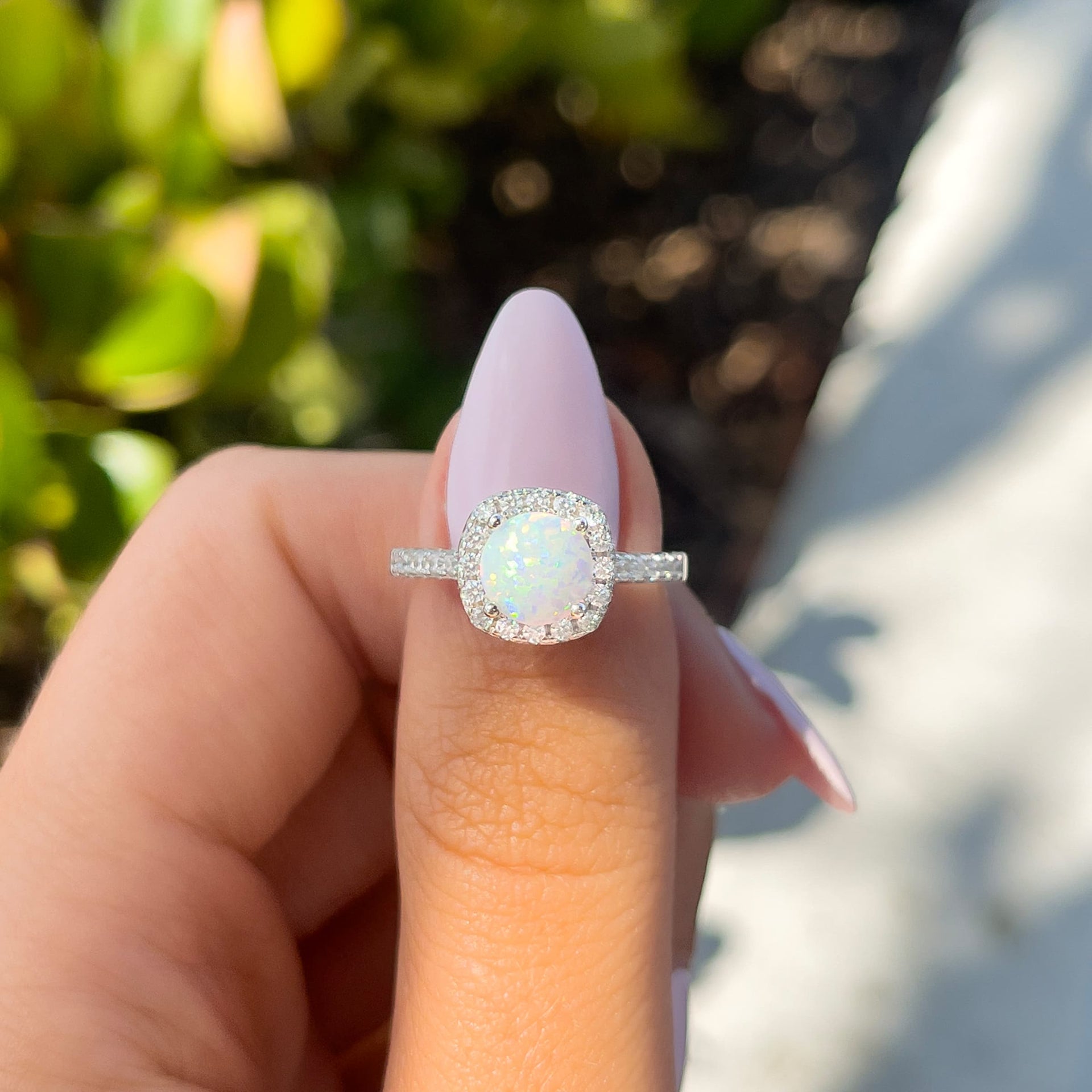 stunning opal halo silver round cut engagement ring on model with light pink nails