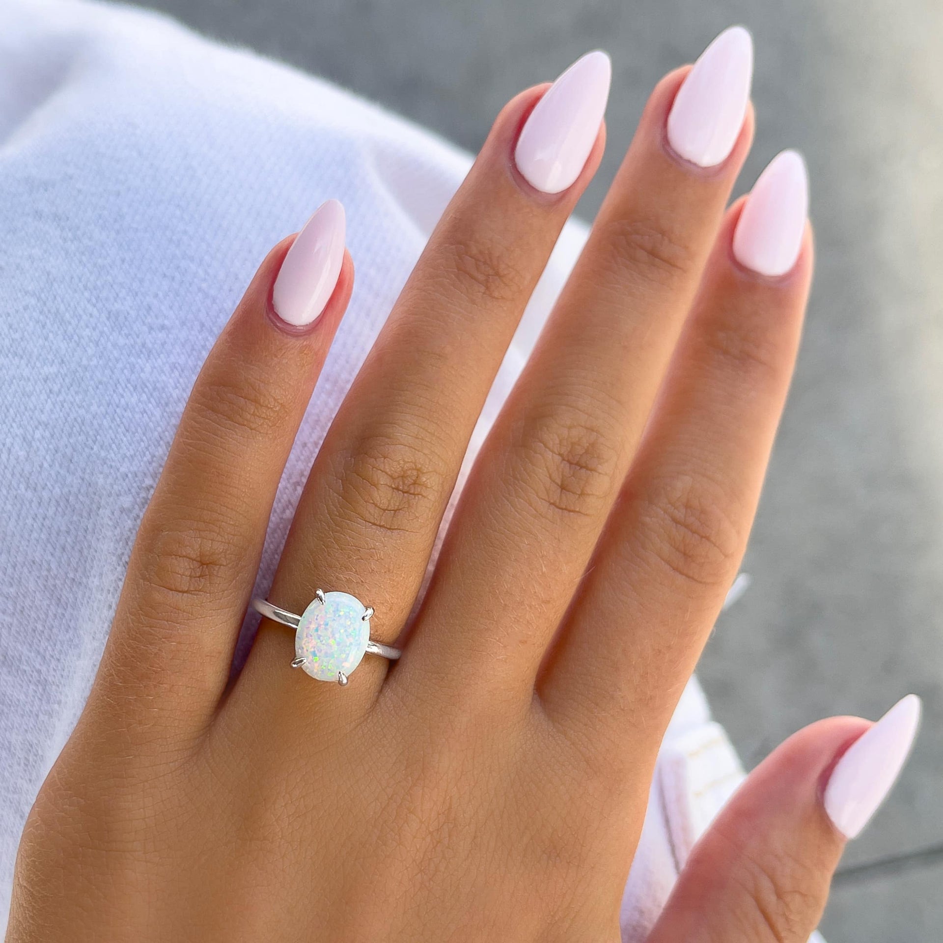 unique simulated opal oval cut solitaire engagement ring with hidden halo on model with light pink nails and white pants