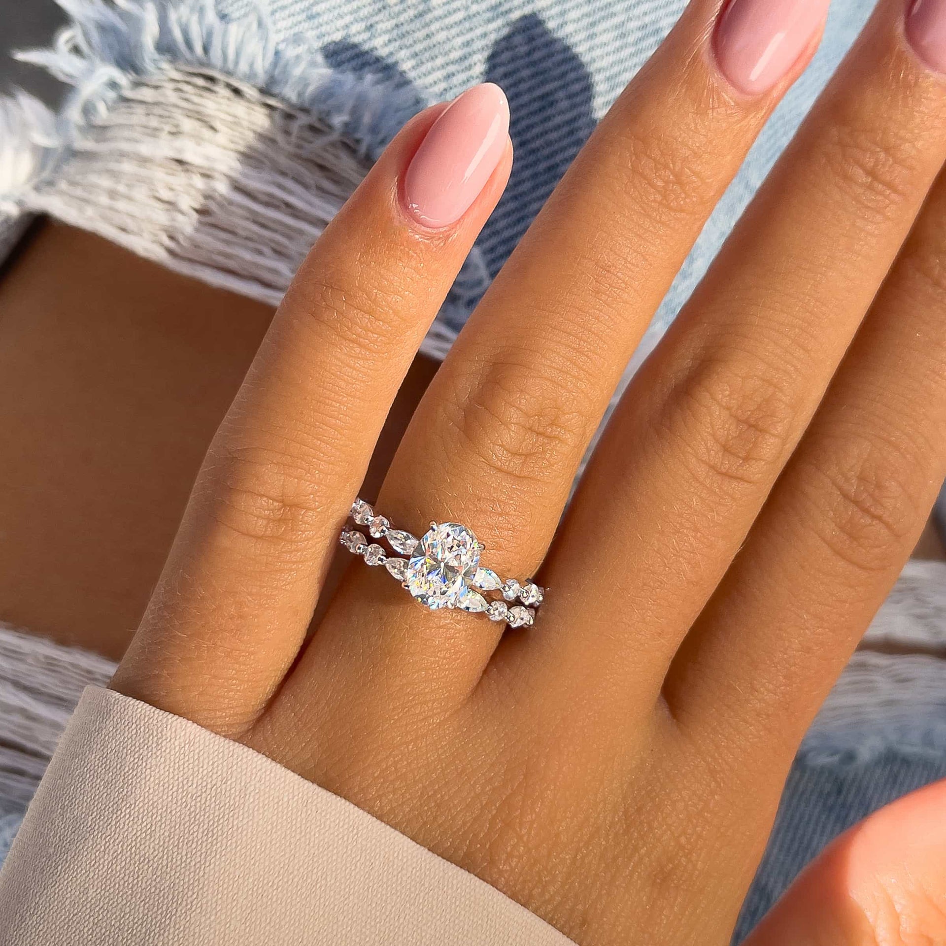 silver wedding band with oval engagement ring on model hand with jeans and tan sleeve