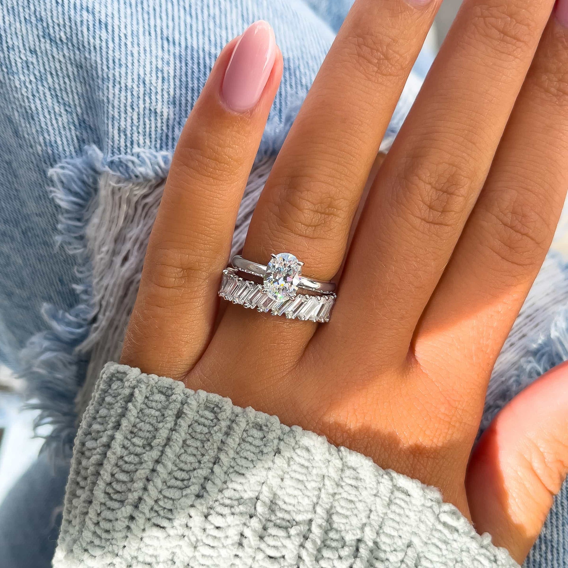 silver 1.5 oval cut solitaire ring paired with baguette band on model with light pink nails and gray sweater