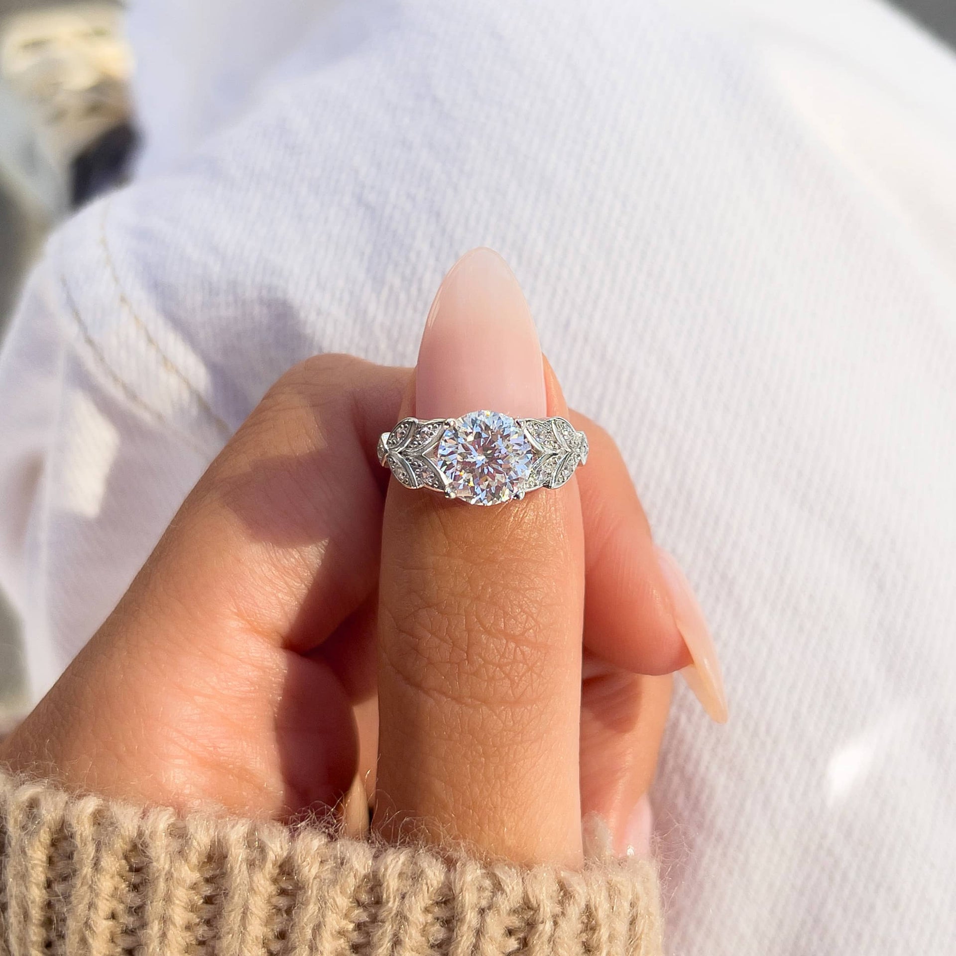 Unique silver round cut engagement ring on model with neutral nails and a tan sweater