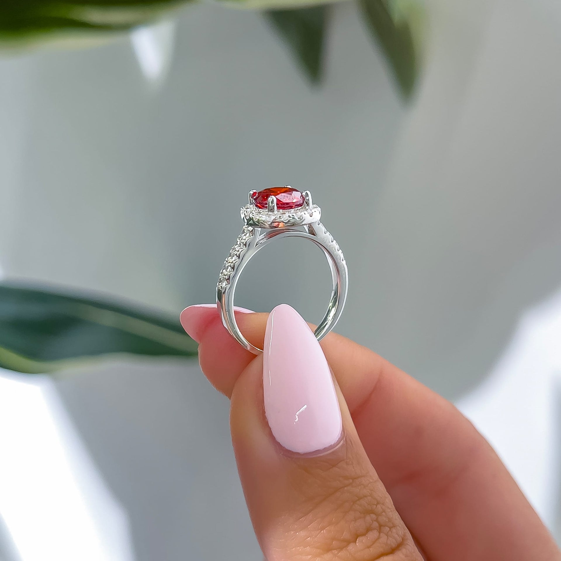 side view of silver halo ruby round cut engagement ring held by model with light pink nails