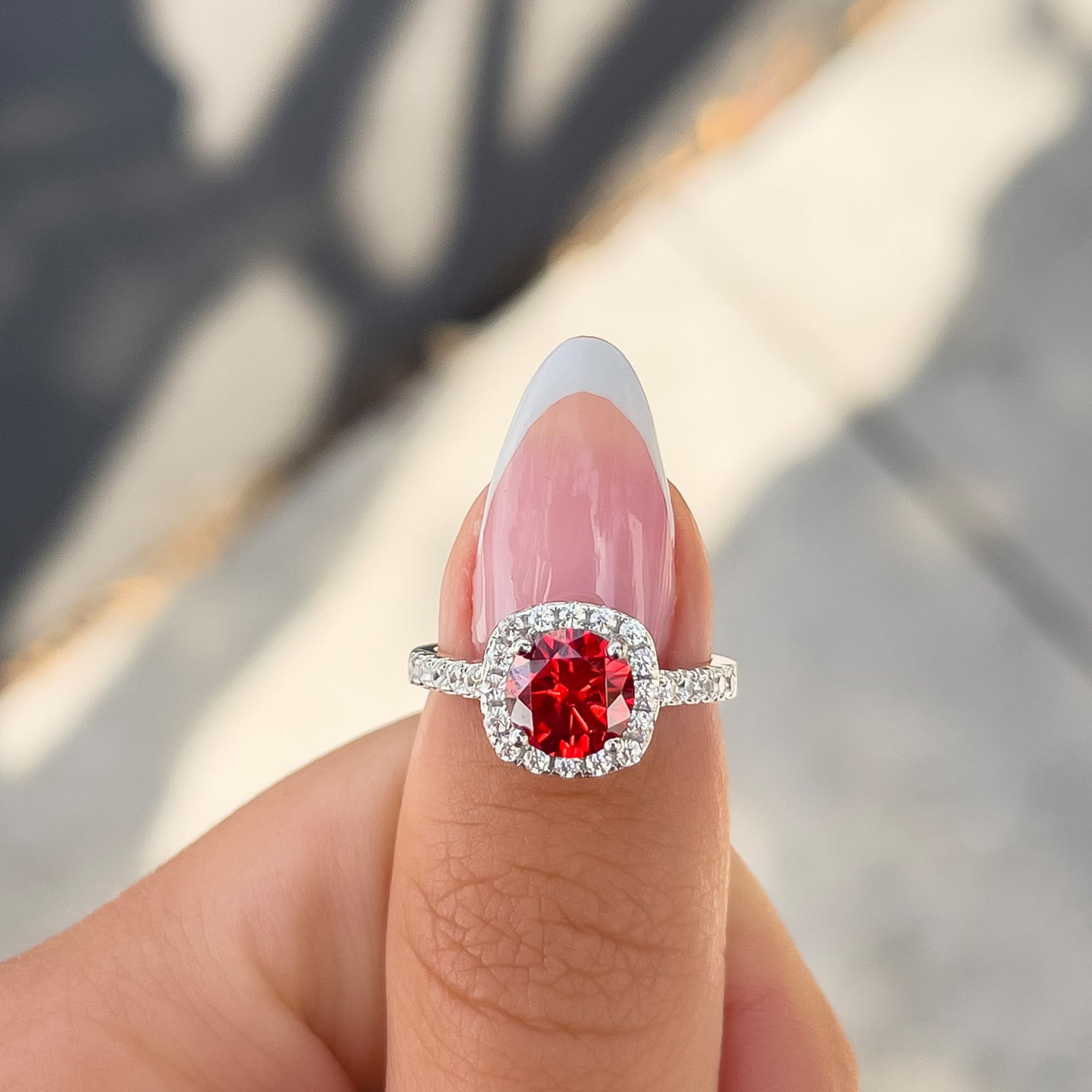 1.5 carat round cut ruby engagement ring on thumb with french tip nail