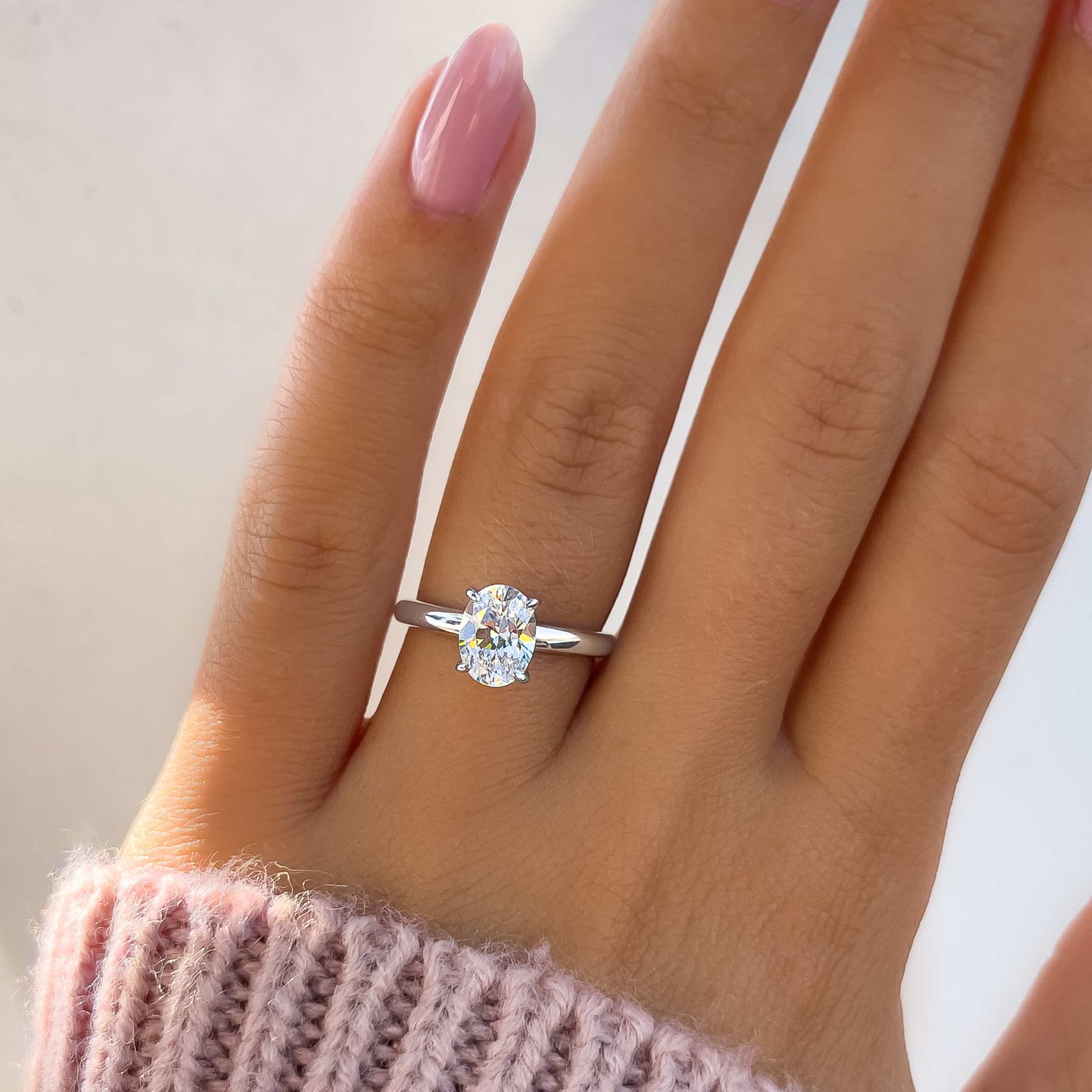 beautiful silver solitaire engagement ring on model's hand with pink nails and pink sweater