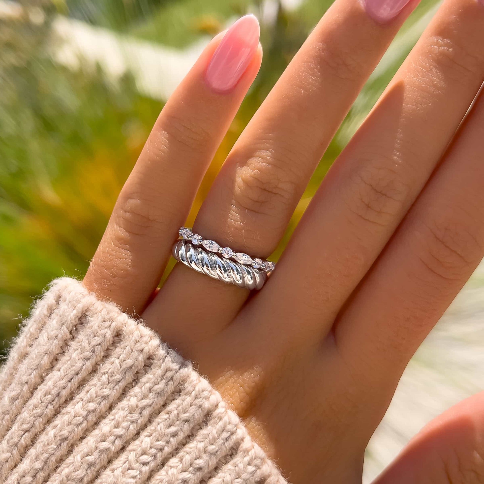 two wedding bands on model's thumb with cream sweater and greenery in the background