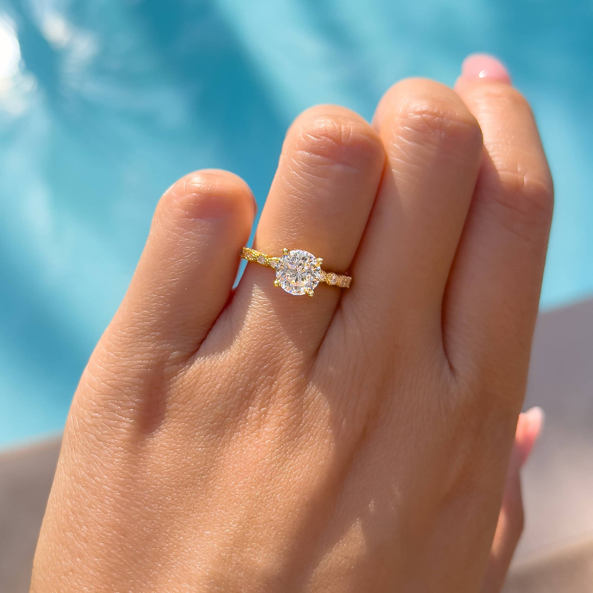 gold round vintage cut engagement ring worn on ladies hand with pool in background