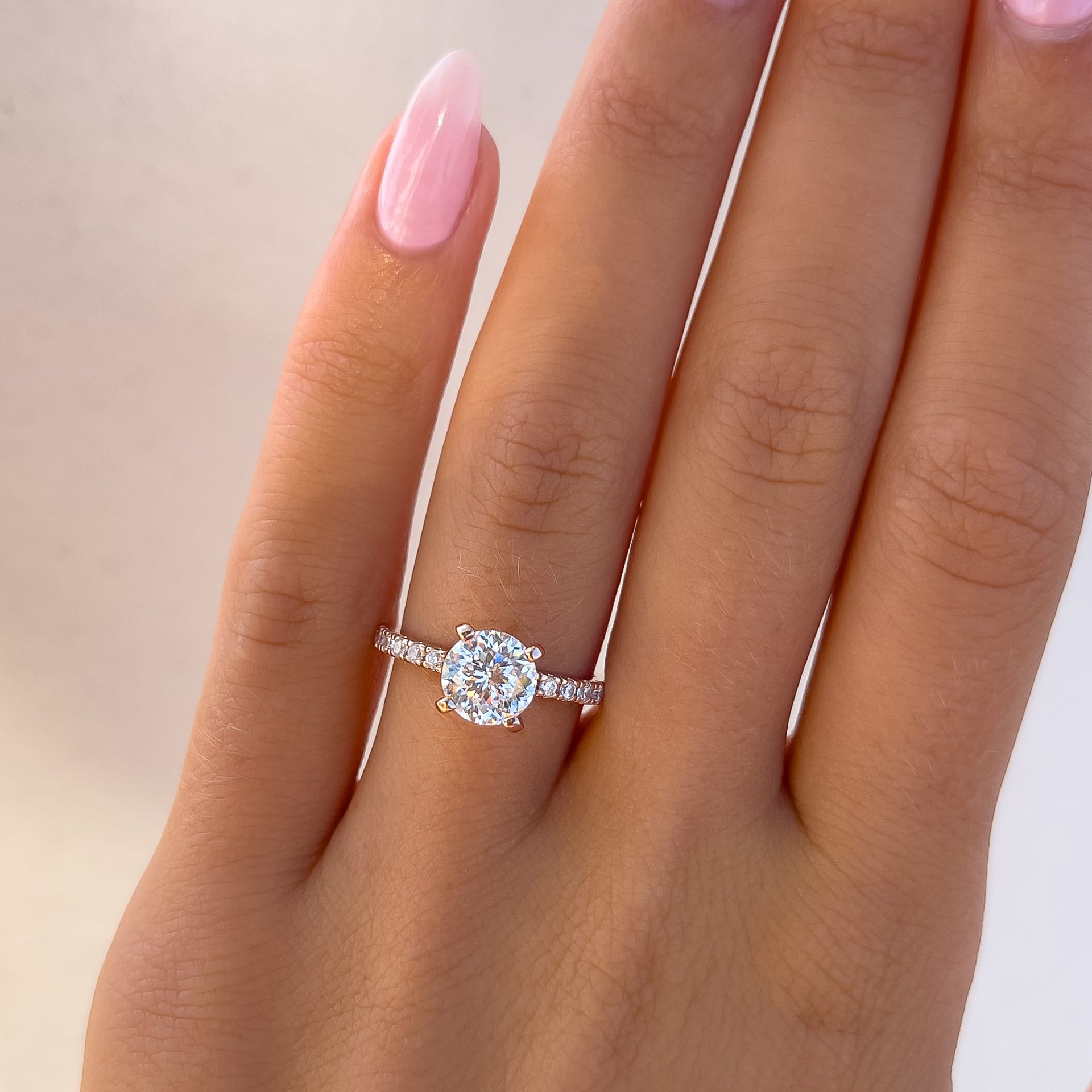 rose gold 1.75 carat round cut engagement ring on model with light pink nails