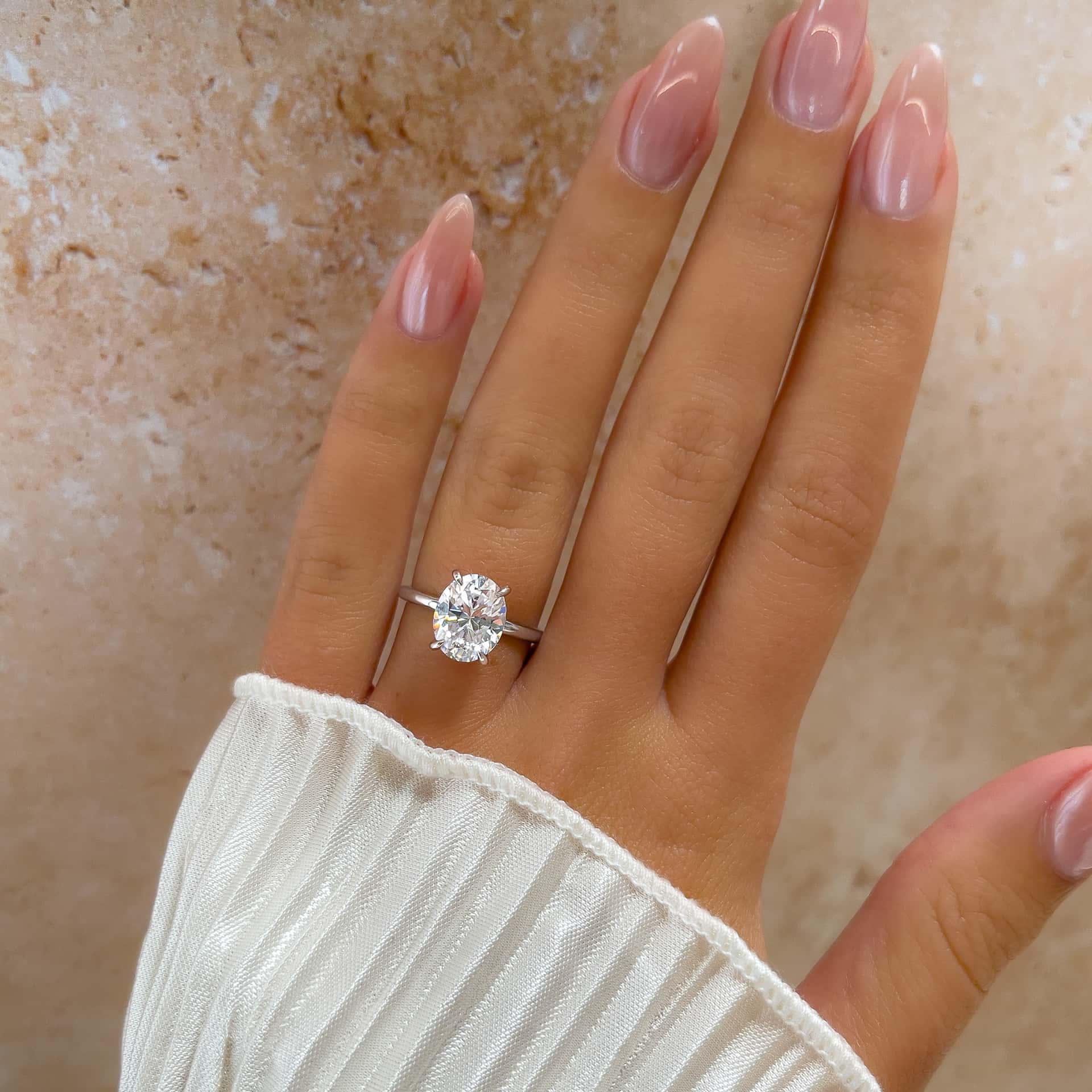 woman with oval silver solitaire engagement ring on hand with pink nails