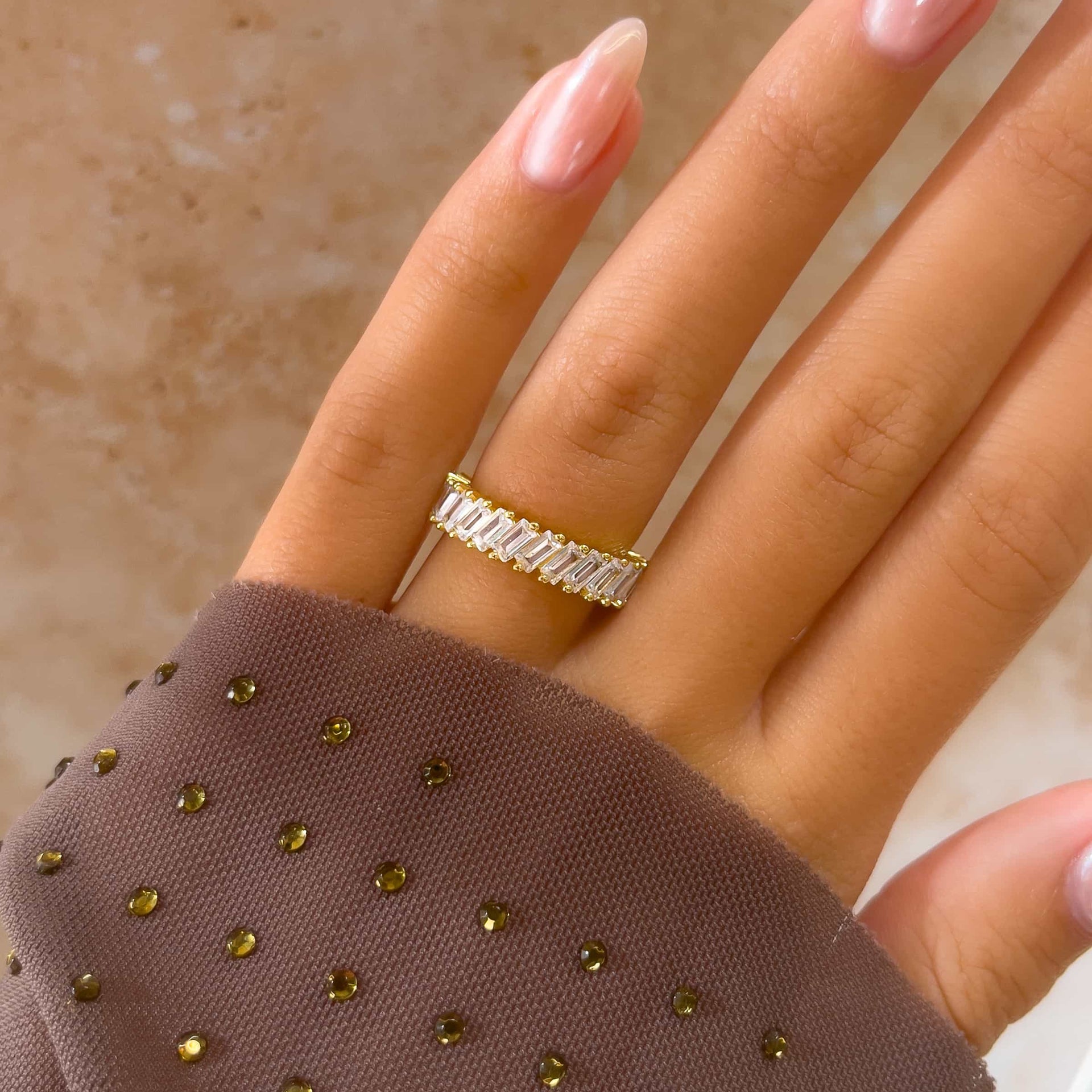 stunning gold baguette wedding band on model's hand with pink nails and purple sleeve