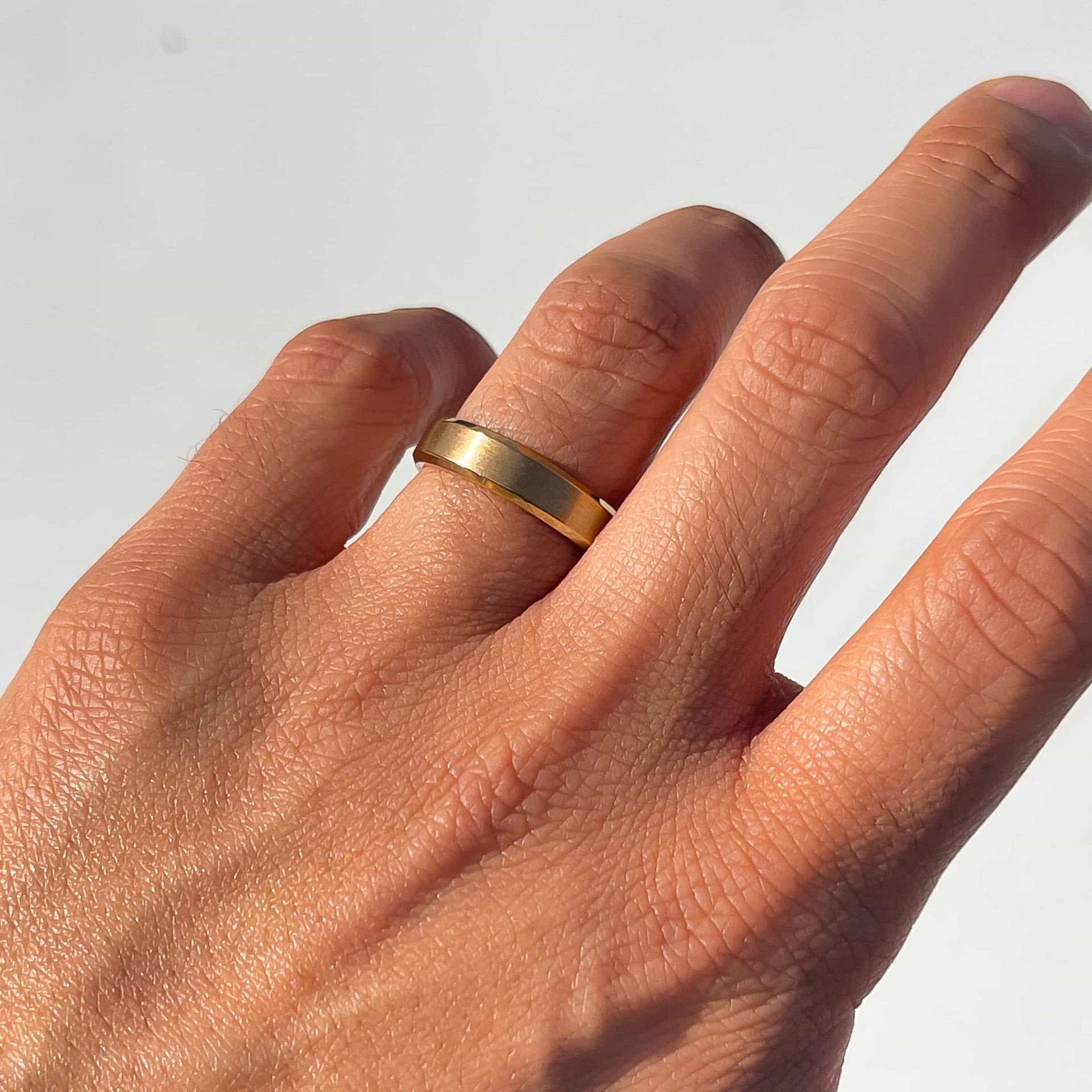 gold wedding band on mens hand with neutral background