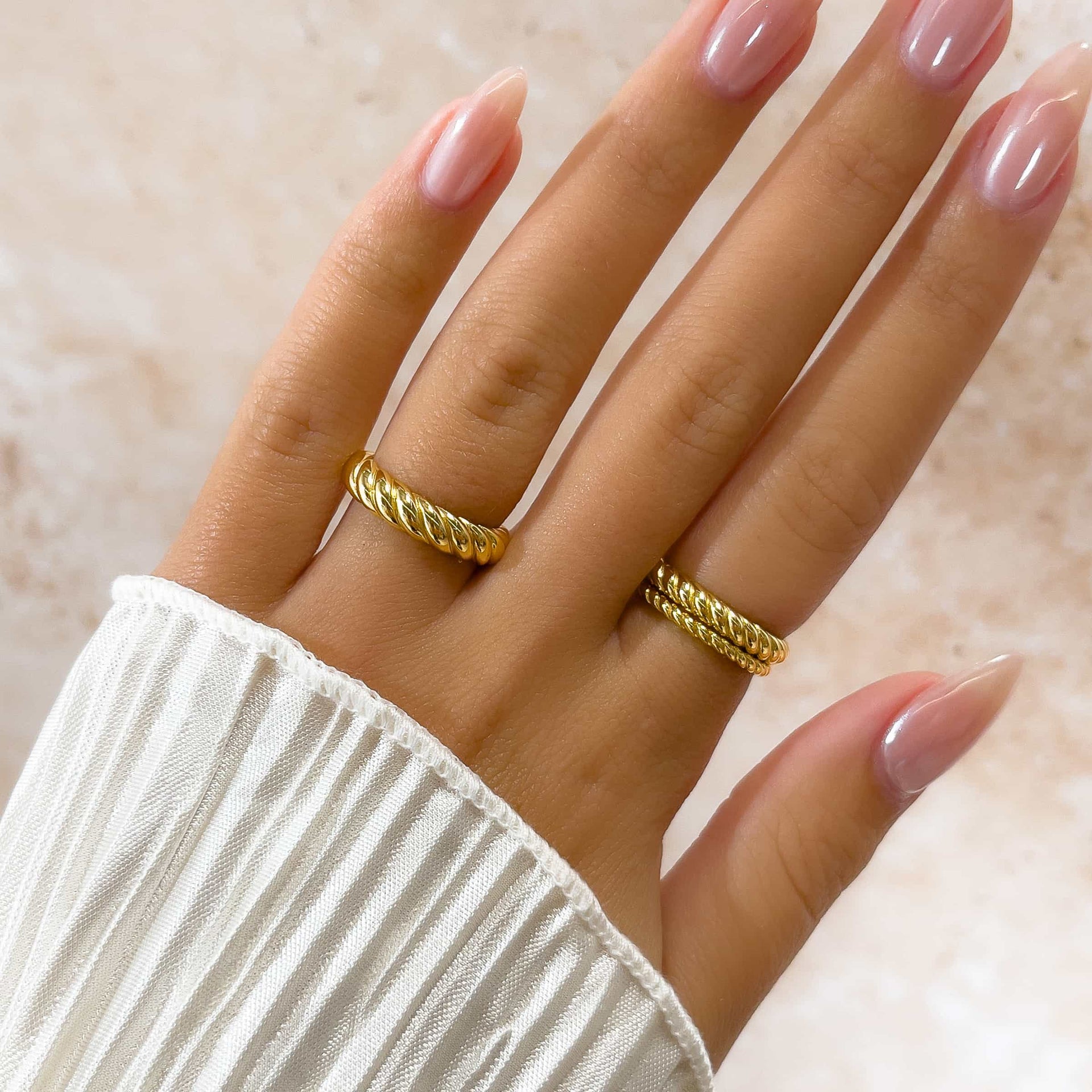 three stunning gold rope wedding rings on model's fingers with pink manicured nails and white shirt sleeve