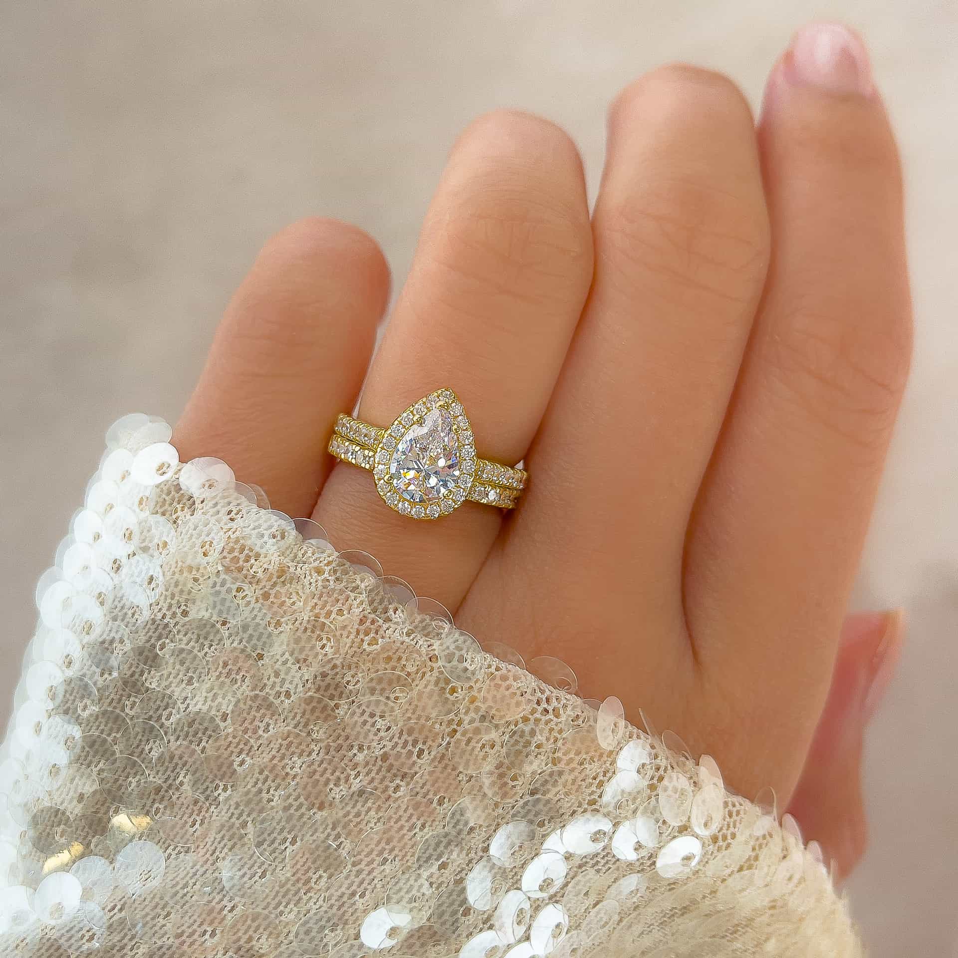 stunning gold 2 carat pear cut halo engagement ring with matching gold half eternity wedding band on model