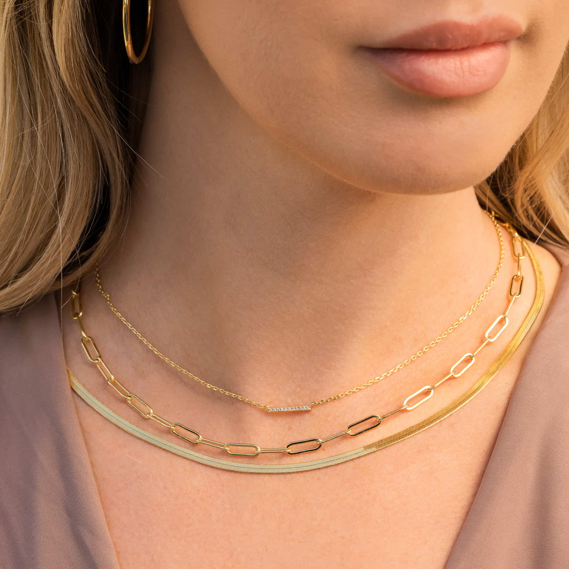 three stunning gold necklaces shown on model's neck with gold hoop earring