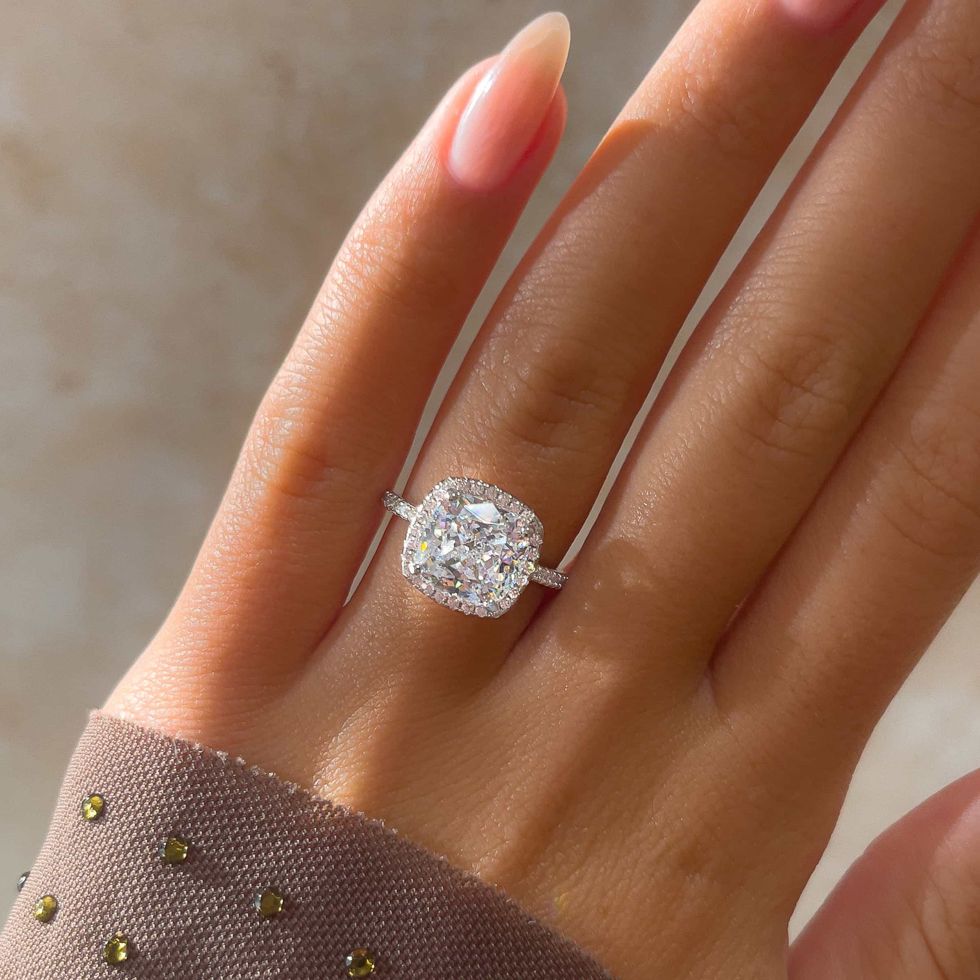 stunning cushion cut silver engagement ring on model's finger with manicured nails and purple shirt