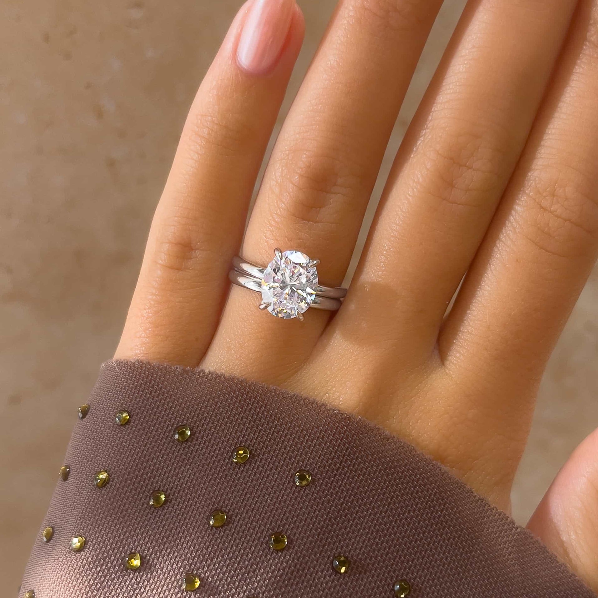 stunning oval cut solitaire engagement ring with silver always wedding band on model's hand with purple shirt and pink nails