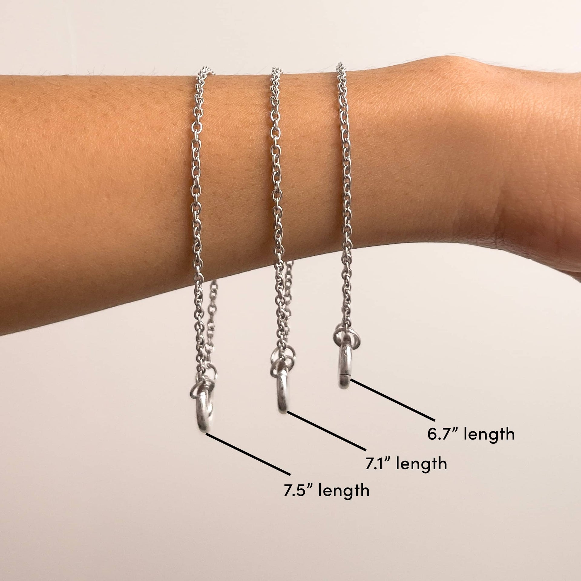 a photo detailing the three different lengths of a silver cable chain charm bracelet we have, worn by a model. from left to right: large (7.5" length), medium (7.1" length), small (67" length)