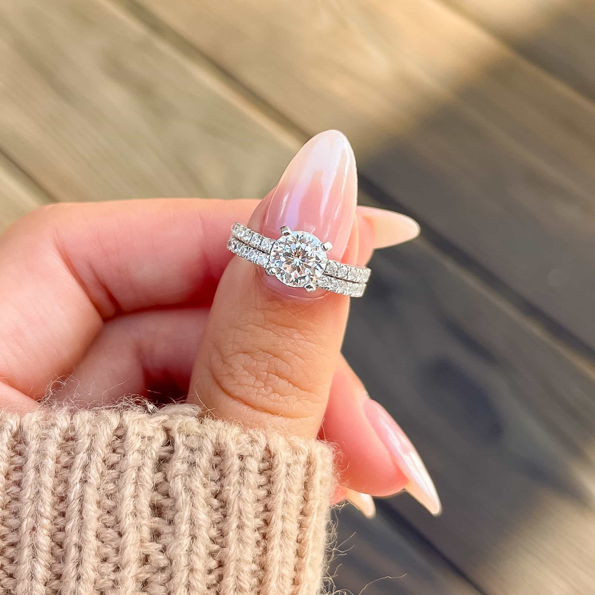 gorgeous round cut silver wedding ring set on woman's finger with tan sweater