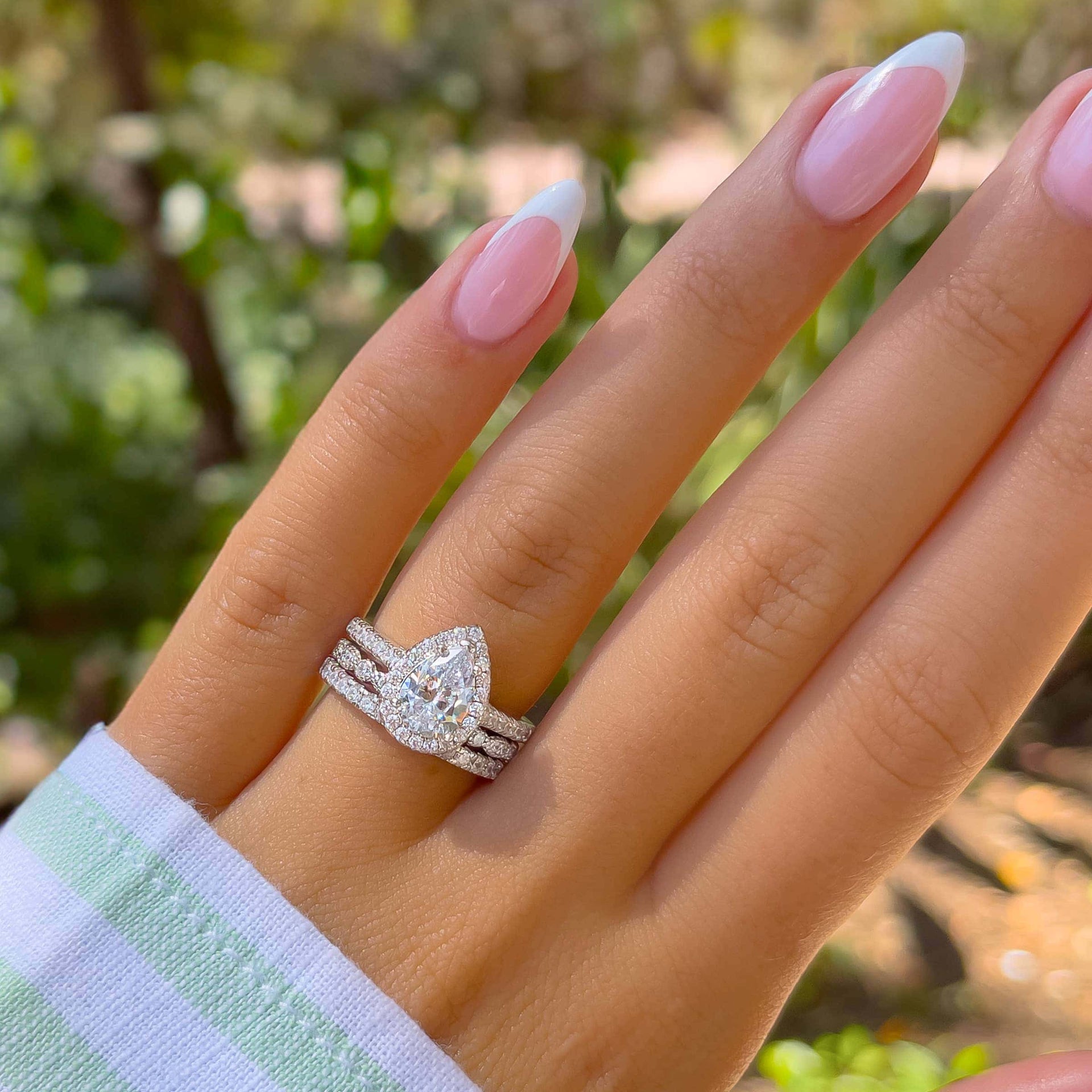 silver pear cut engagement ring with vintage wedding band and eternity wedding band with greenery in background