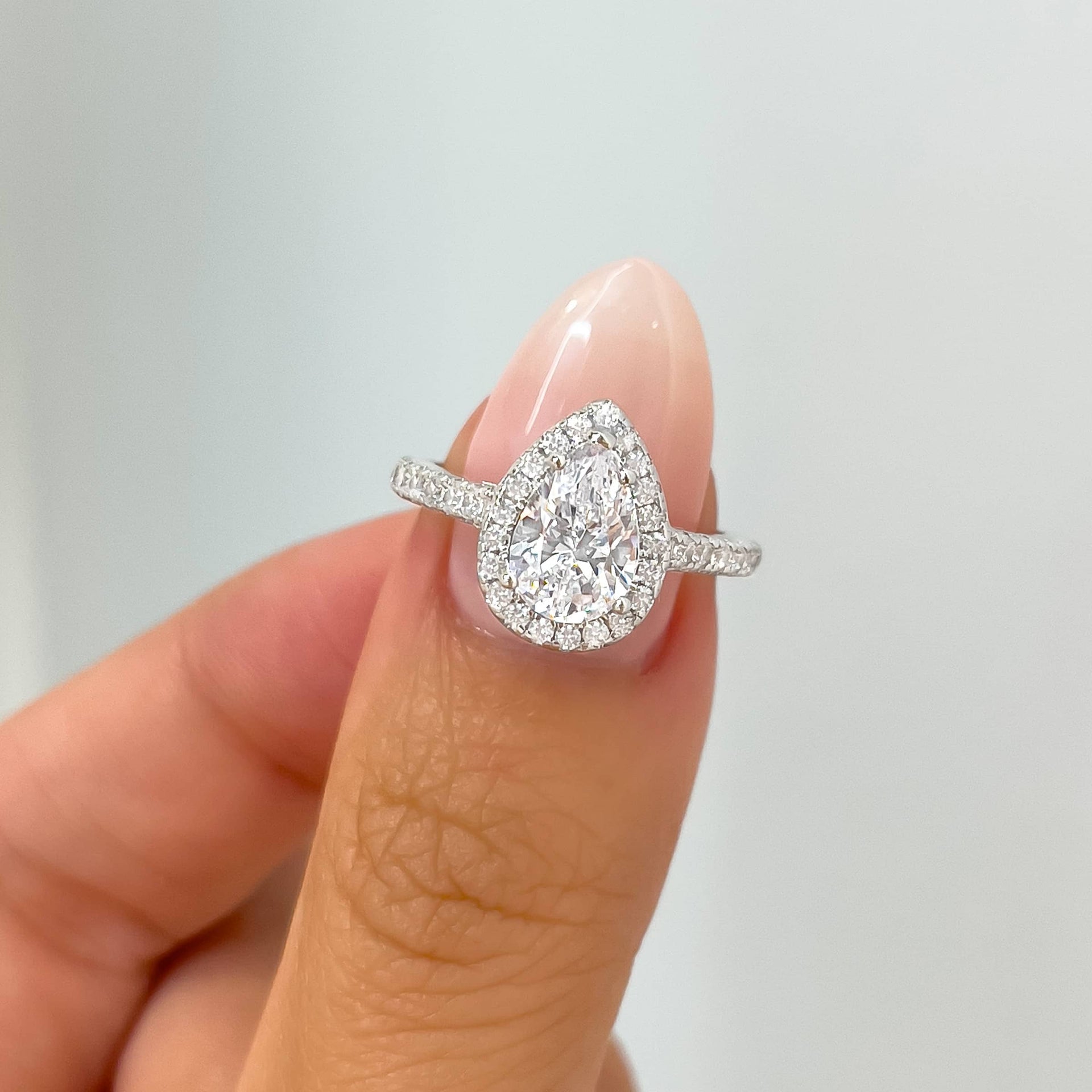 stunning 2-carat pear engagement ring on ladies thumb with pink nail
