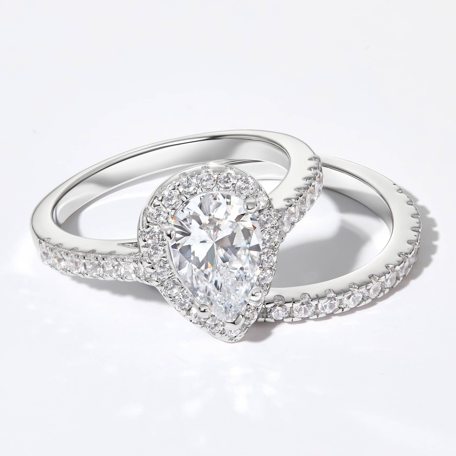flatlay of 2 ct silver pear cut engagement ring with matching half eternity band on white background