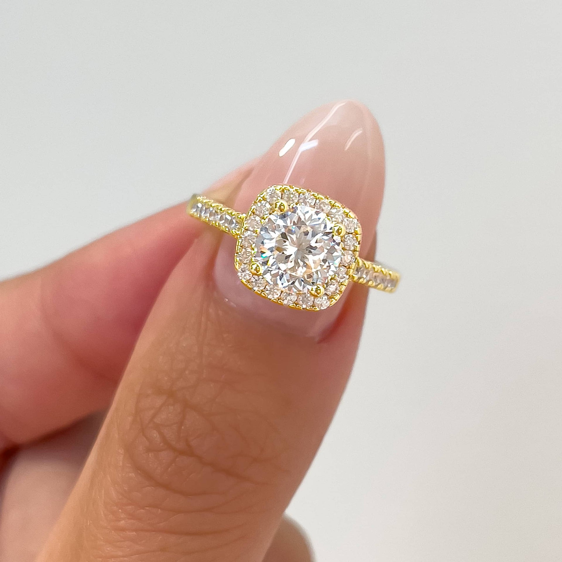woman pinching 1.5 ct cushion cut engagement ring shown in gold with white background