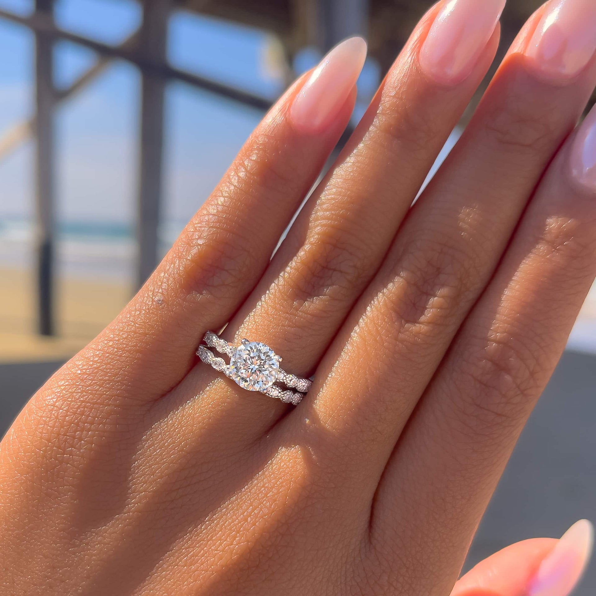 woman wearing 1.5 ct affordable engagement ring with complimentary wedding band by pier and ocean