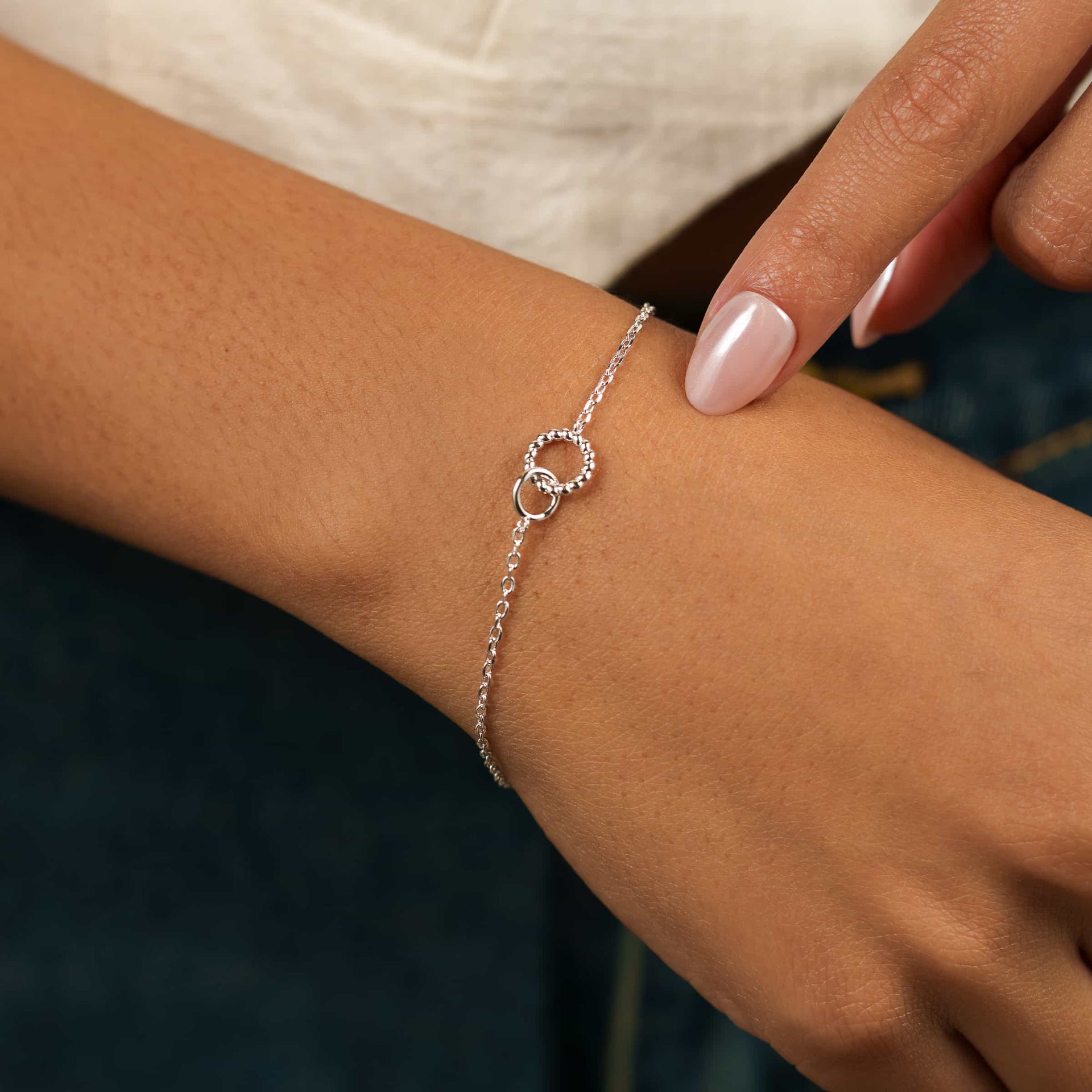 a silver dainty bracelet with minimal interlocking hoop detail on a white background worn by model