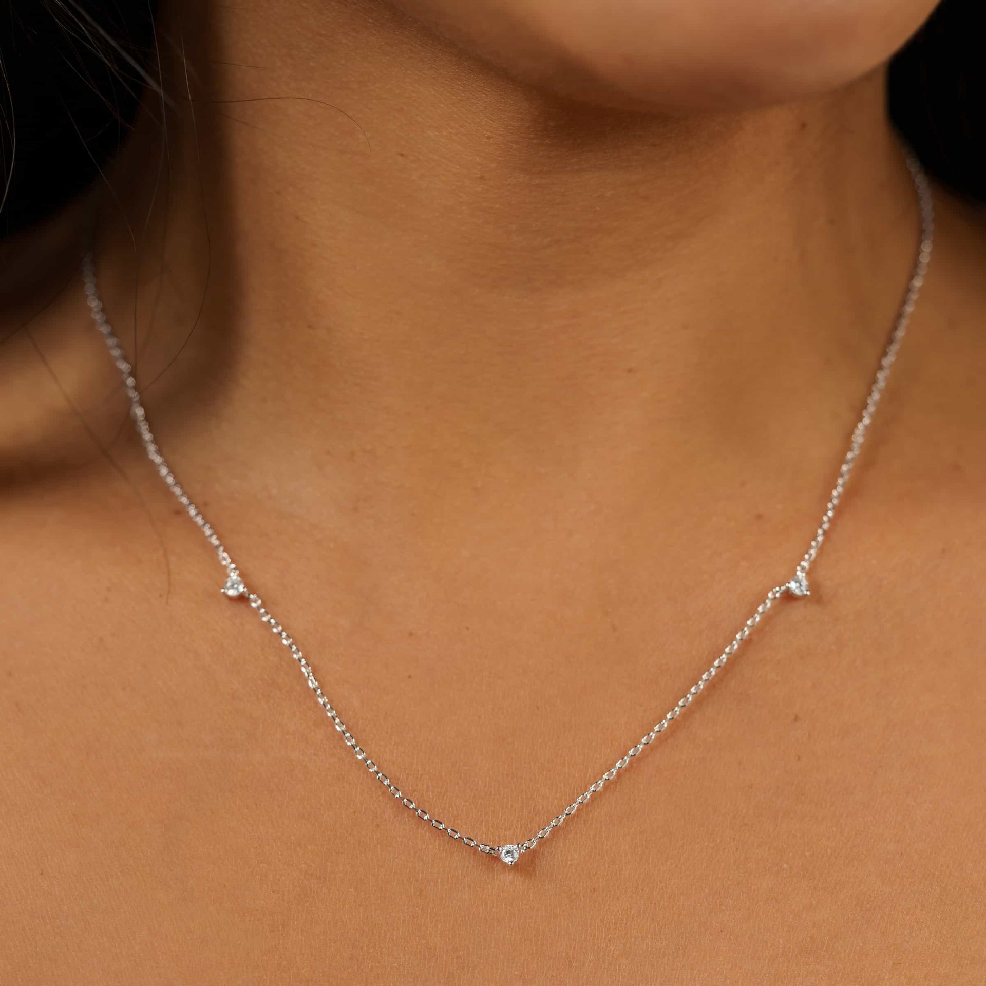 a simple silver necklace with 3 dainty round stones along its chain, worn by model