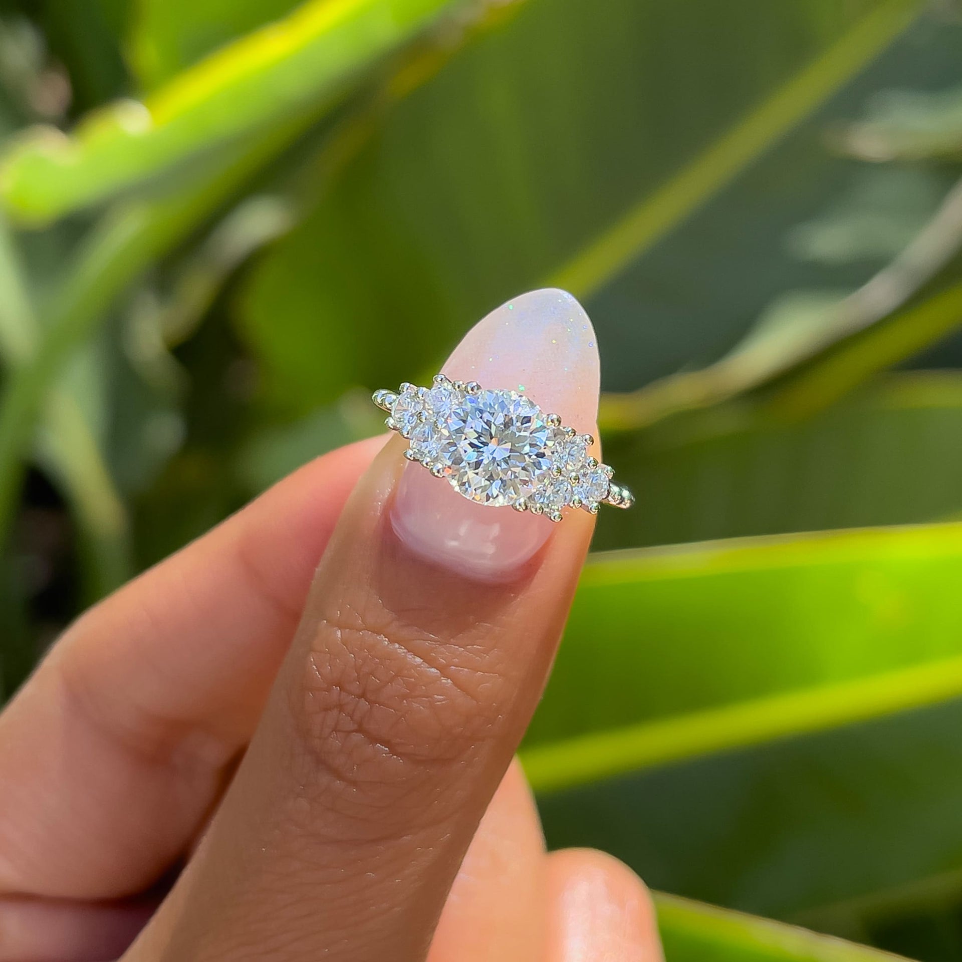 unique silver round cut engagement ring held by model with sparkly light pink nails