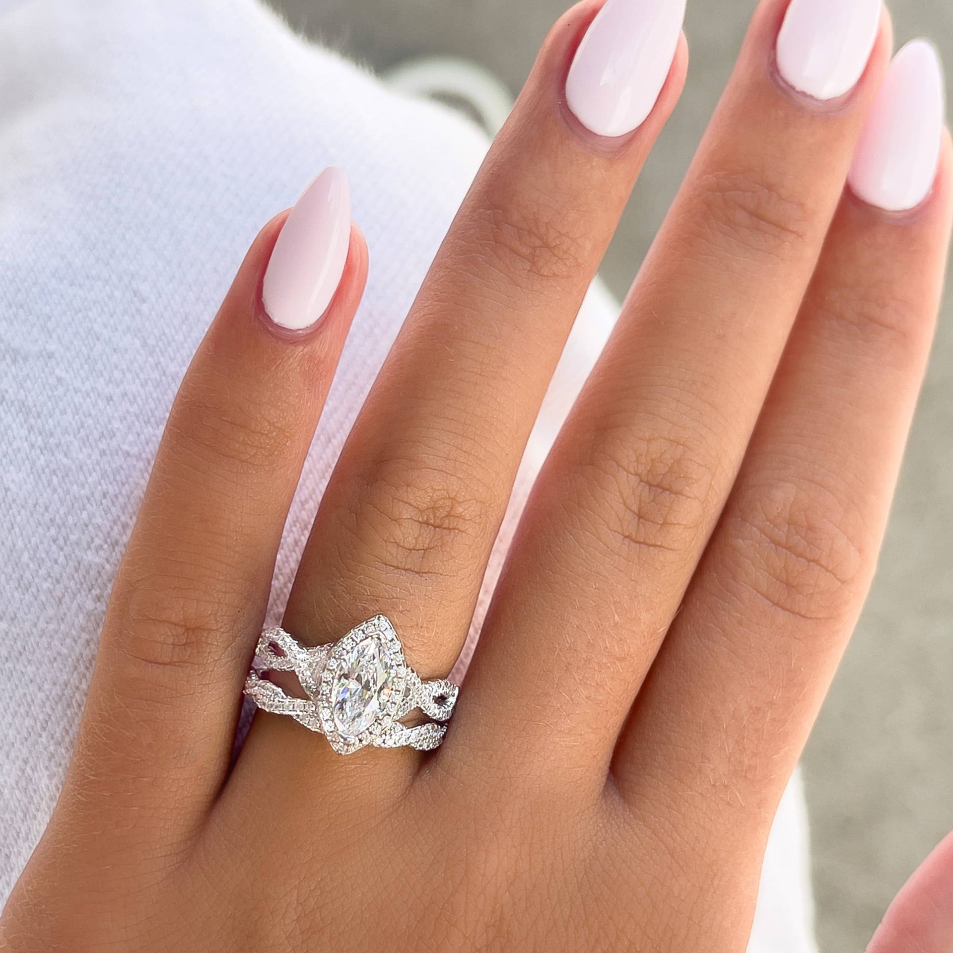 silver marquise cut vintage engagement ring paired with twisting wedding band on model with light pink nails