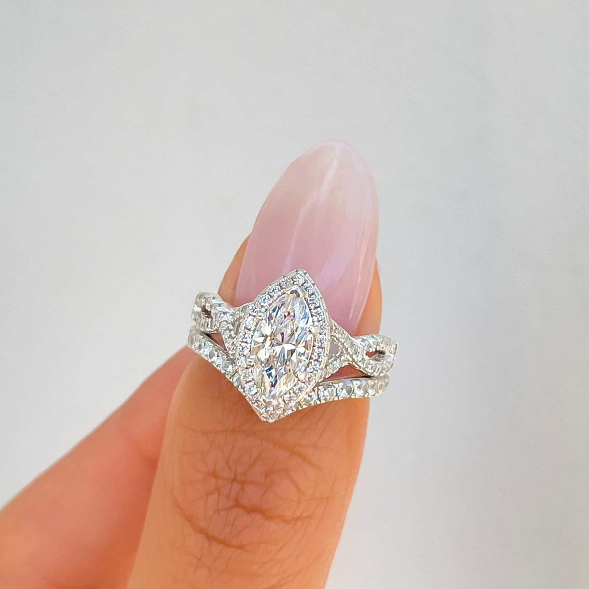 silver marquise cut halo vintage engagement ring with complementary v-shaped band on model with light pink nail