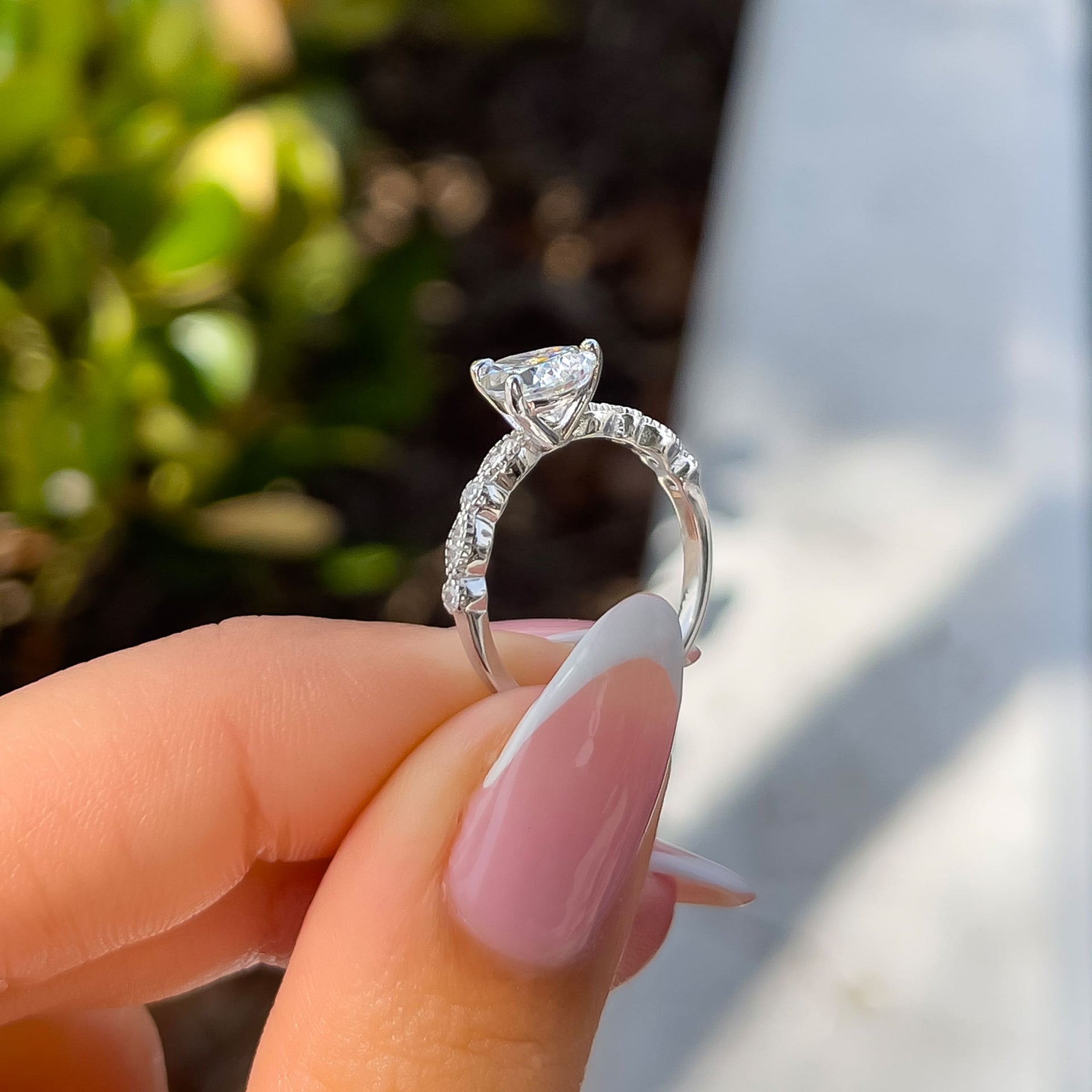 side profile of silver pear cut vintage engagement ring held by female model with french tip nails